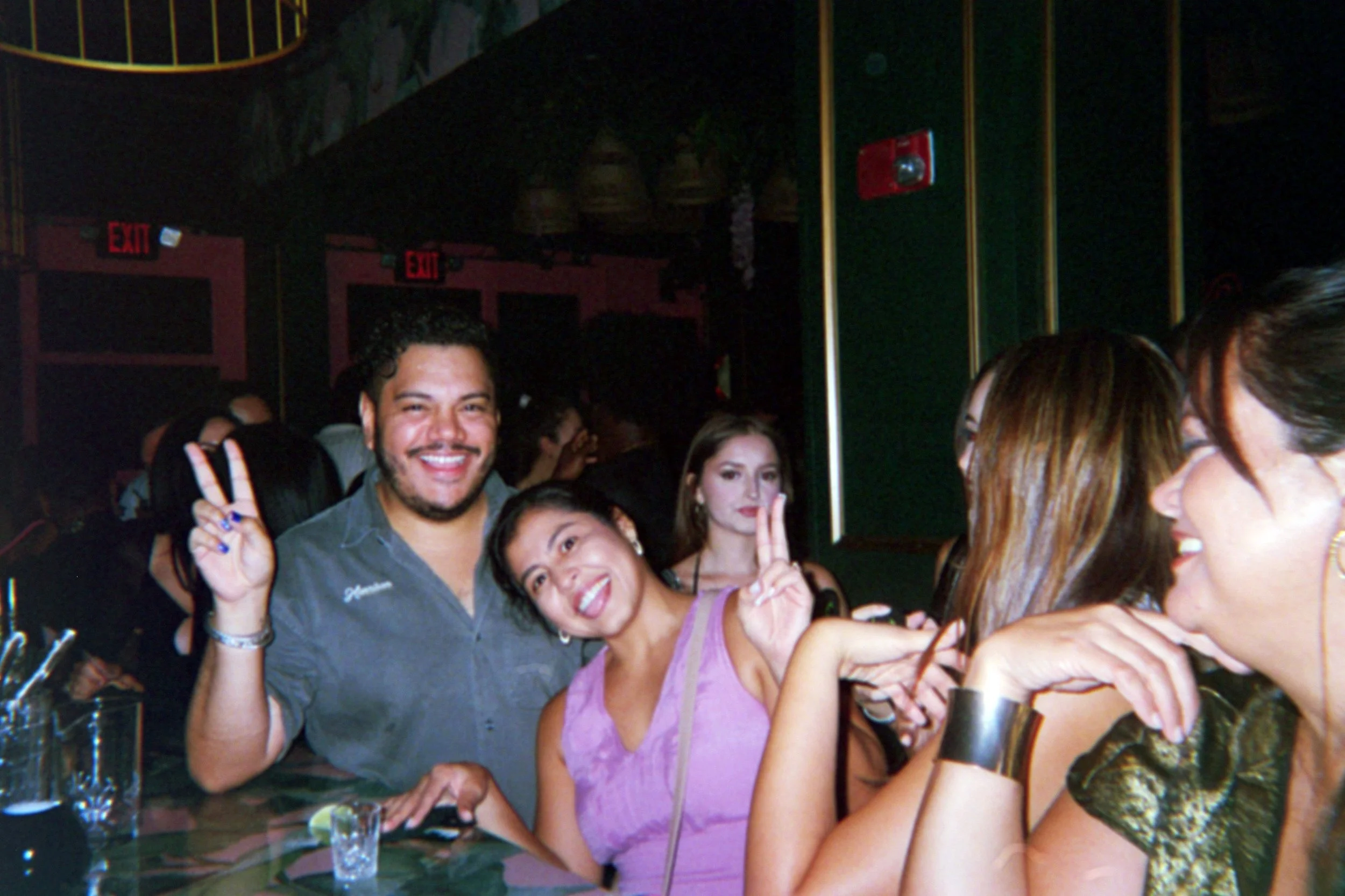 Group of friends in a bar, smiling, posing with peace signs, and having a good time.