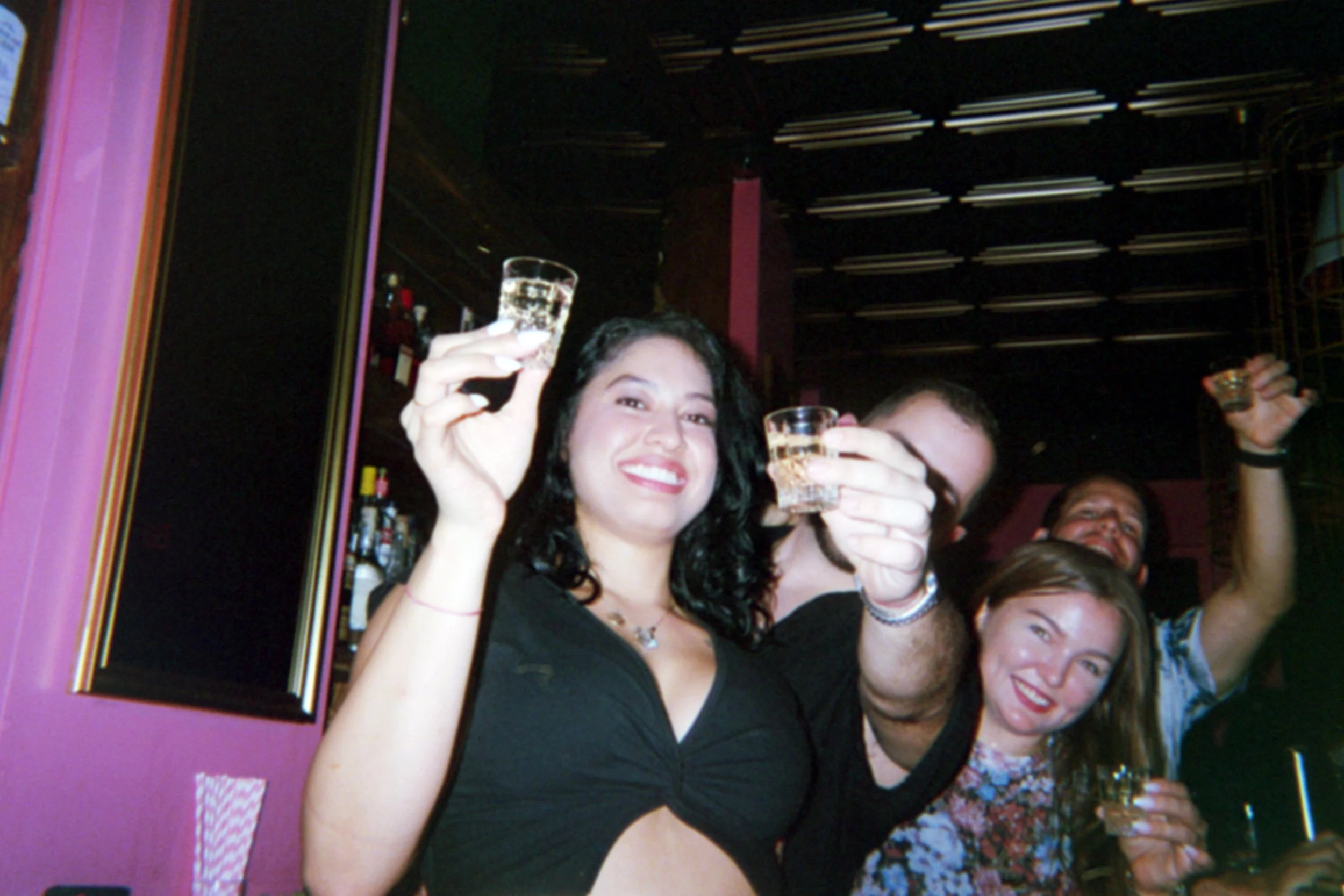 Group of friends celebrating with drinks at a bar or club, smiling and raising glasses.