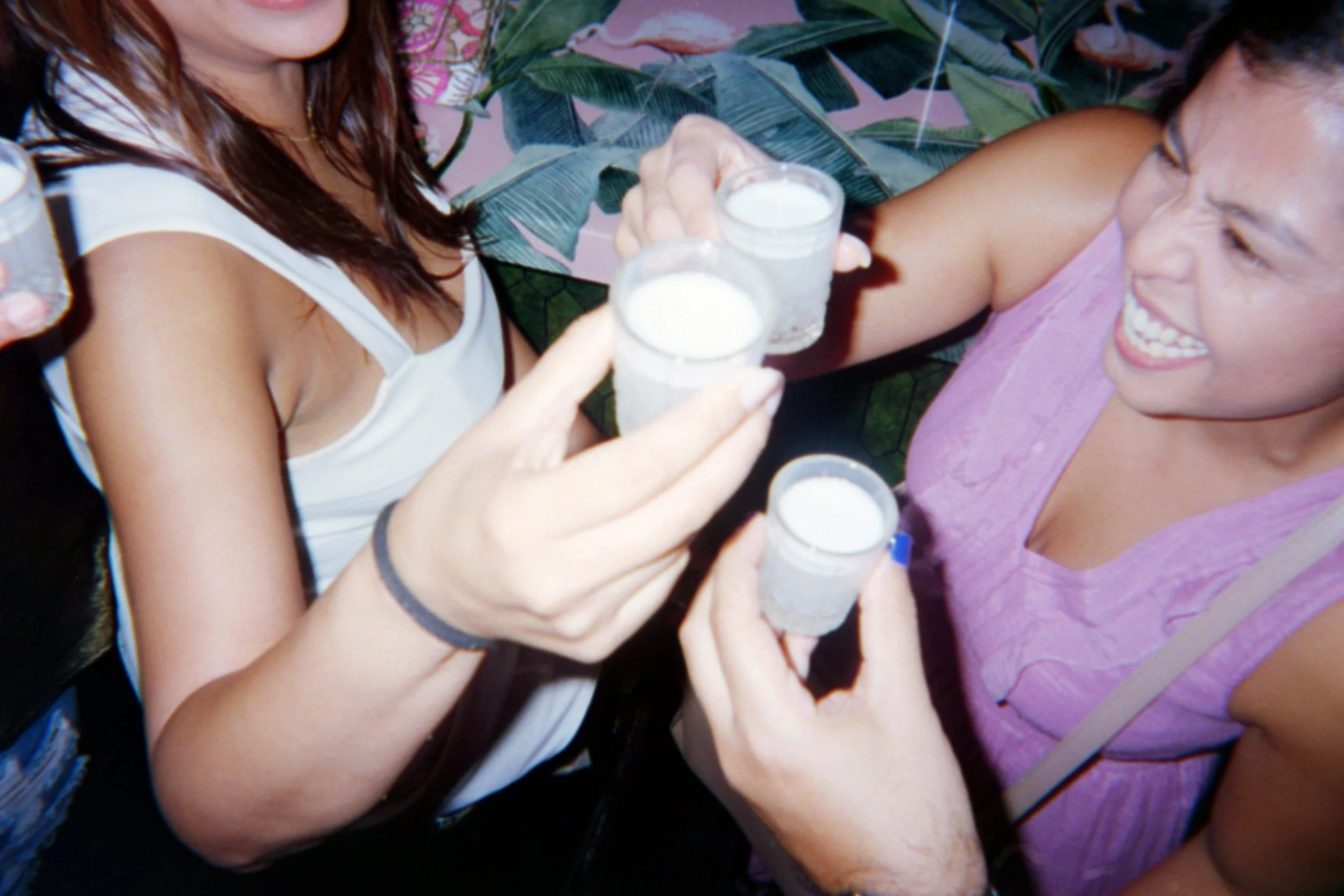 Two women clinking glasses filled with a white beverage, smiling during a celebration.