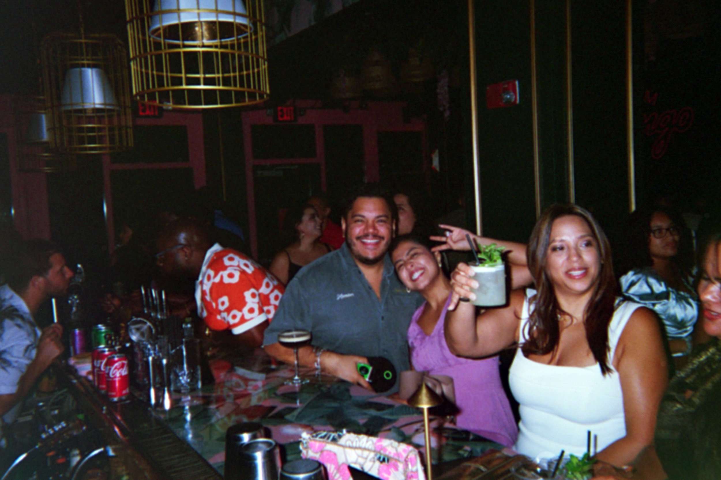 People smiling and enjoying drinks at a bar in a lively nightlife setting.