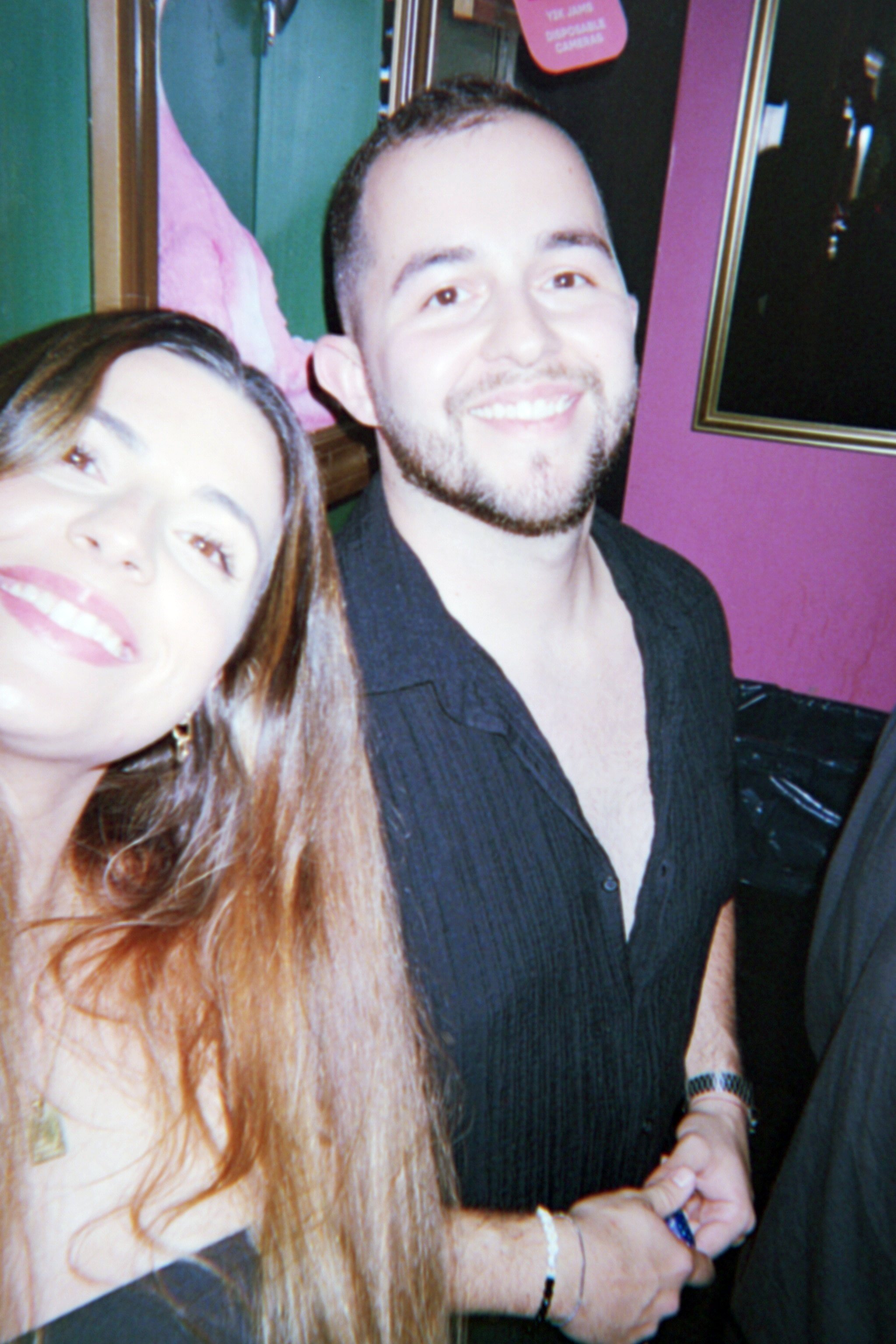 Smiling man and woman taking a selfie in an indoor setting with pink and green walls.
