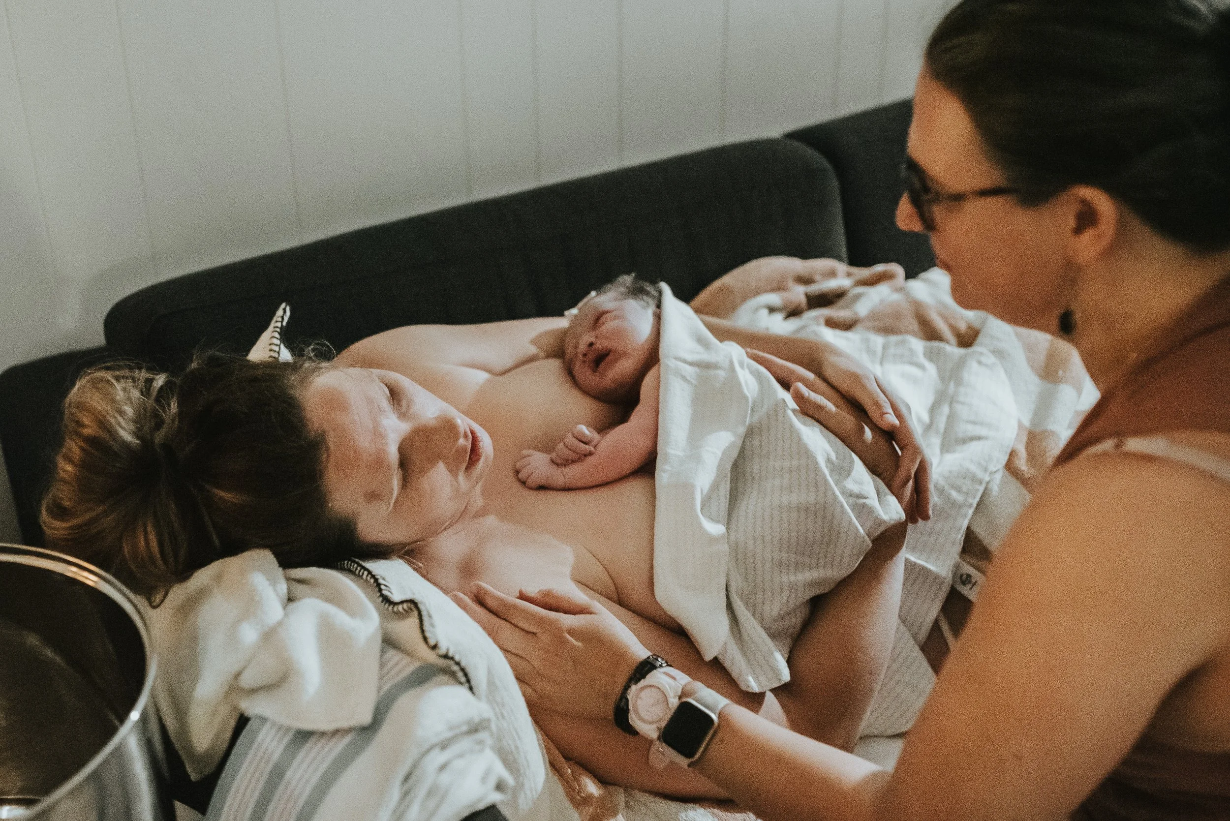 Woman-holds-her-baby-after-birth-her-midwife-looks-at-her-with-reassurance-that-all-is-well.