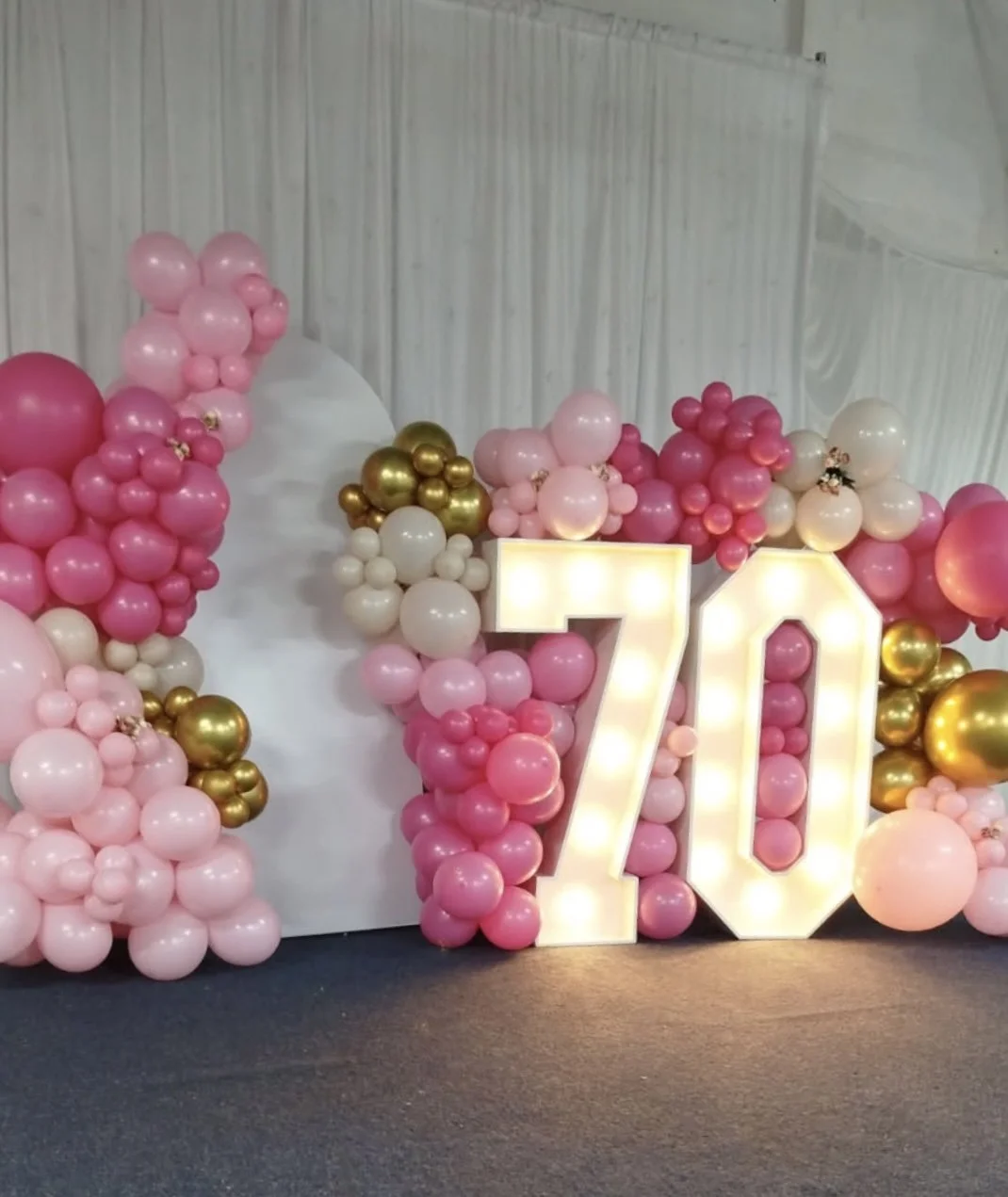 Large illuminated number '70' surrounded by pink, white, and gold balloons, likely for a 70th birthday celebration.