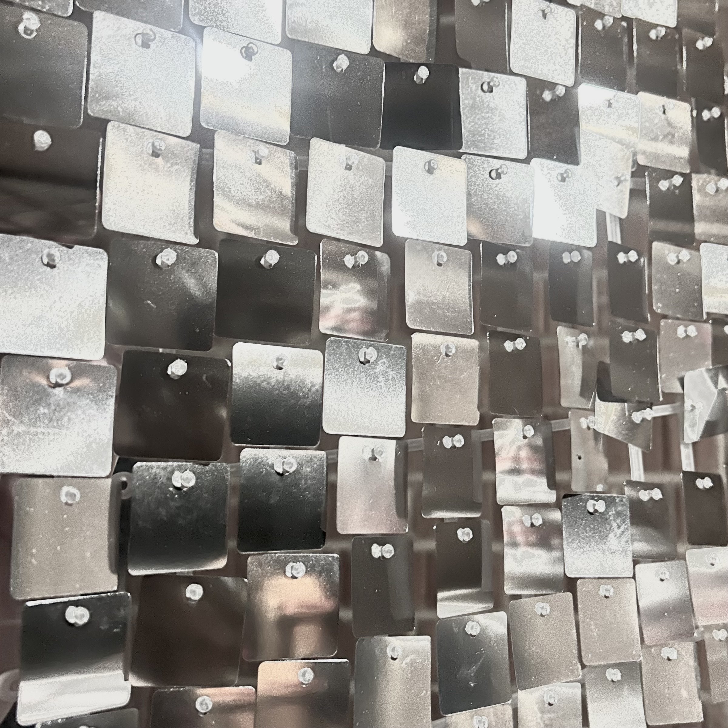 Close-up of a decorative hanging piece made of numerous small, square, metallic tiles connected by small bolts.