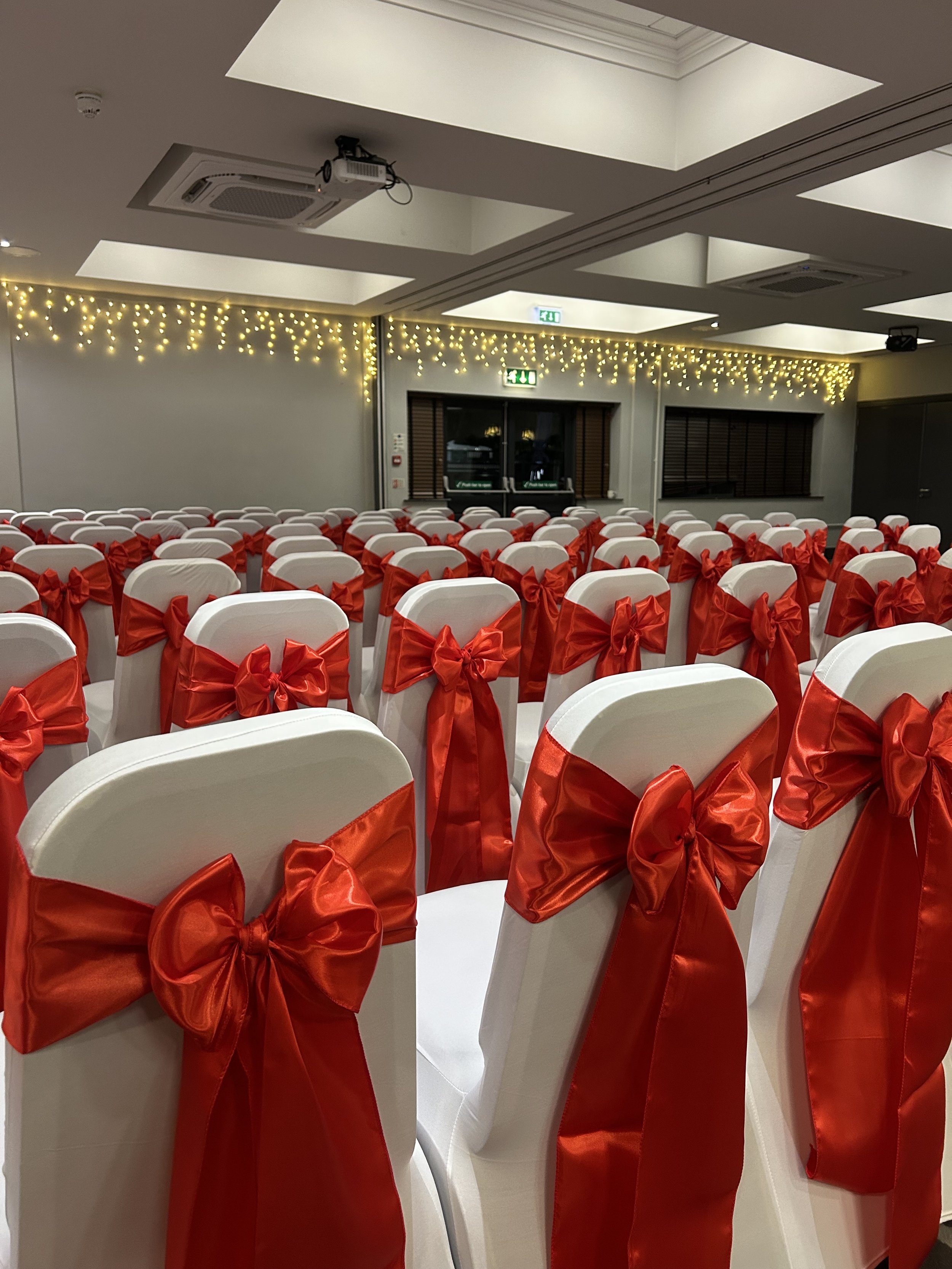 Chairs decorated with red bows arranged in rows in a decorated event hall for a celebration or wedding.
