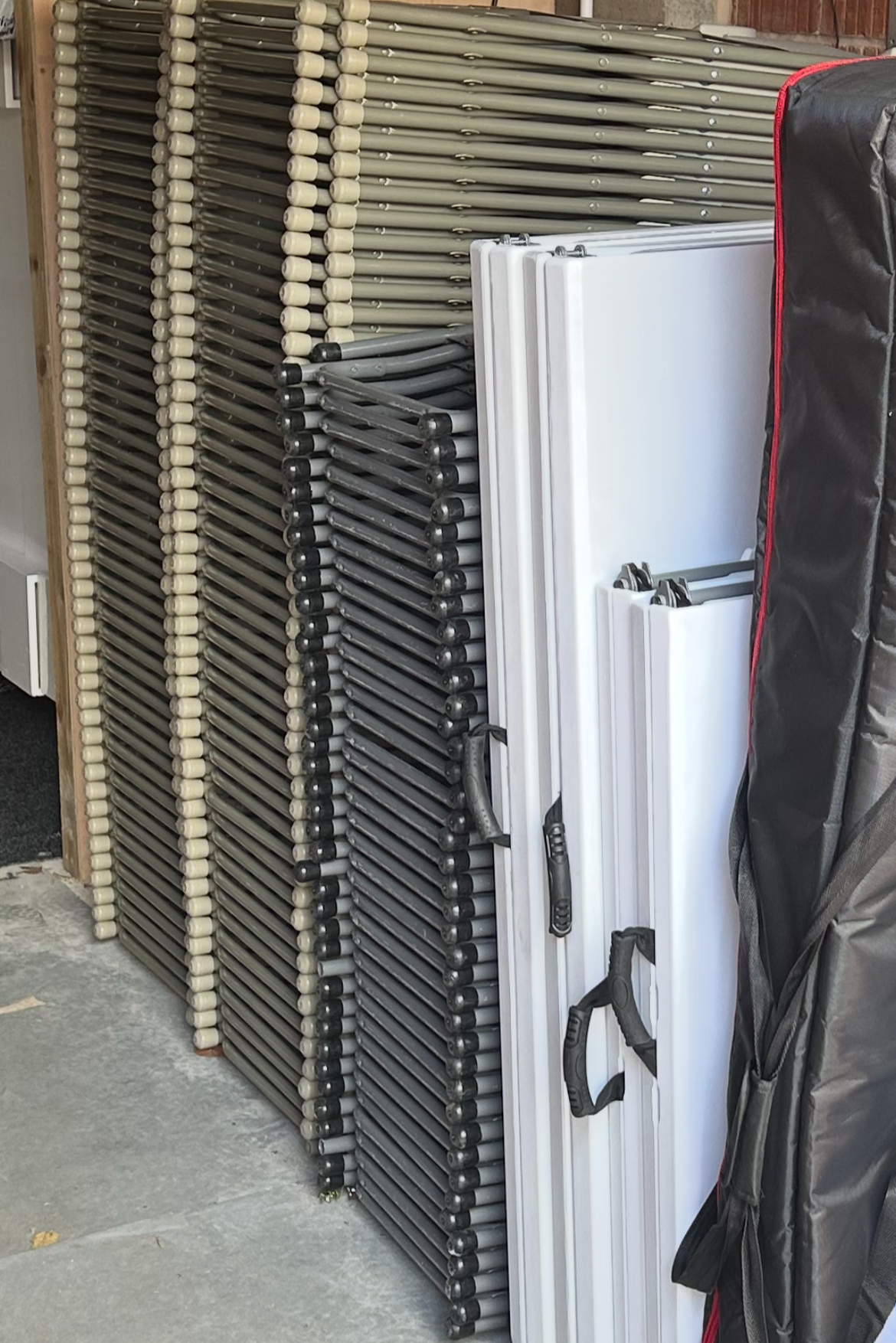Stacked folding tables with black and white legs leaning against a wooden wall in a storage area.