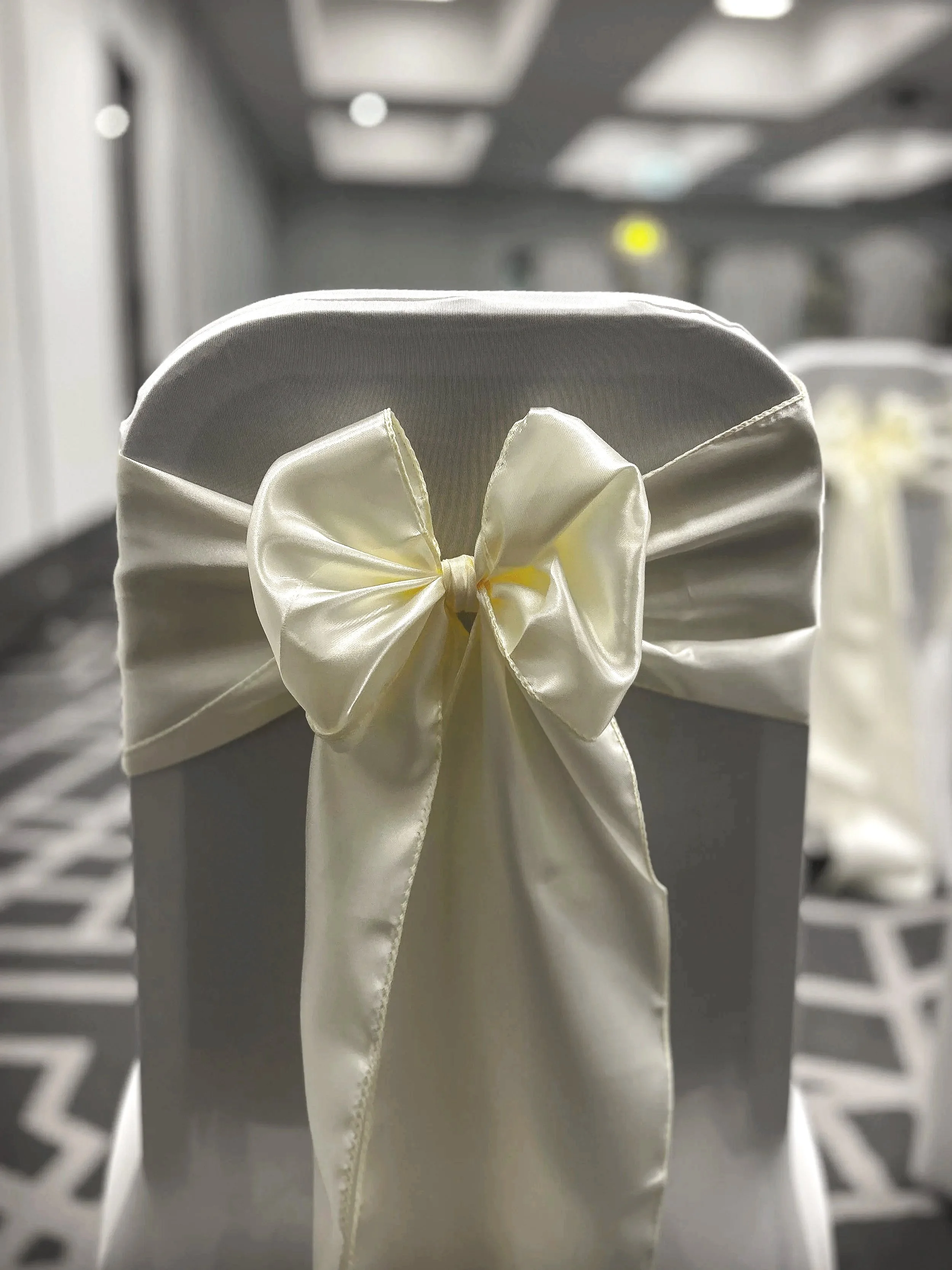 Close-up of a white satin pillow with a satin bow, set against a blurred background of a laundry room or closet.