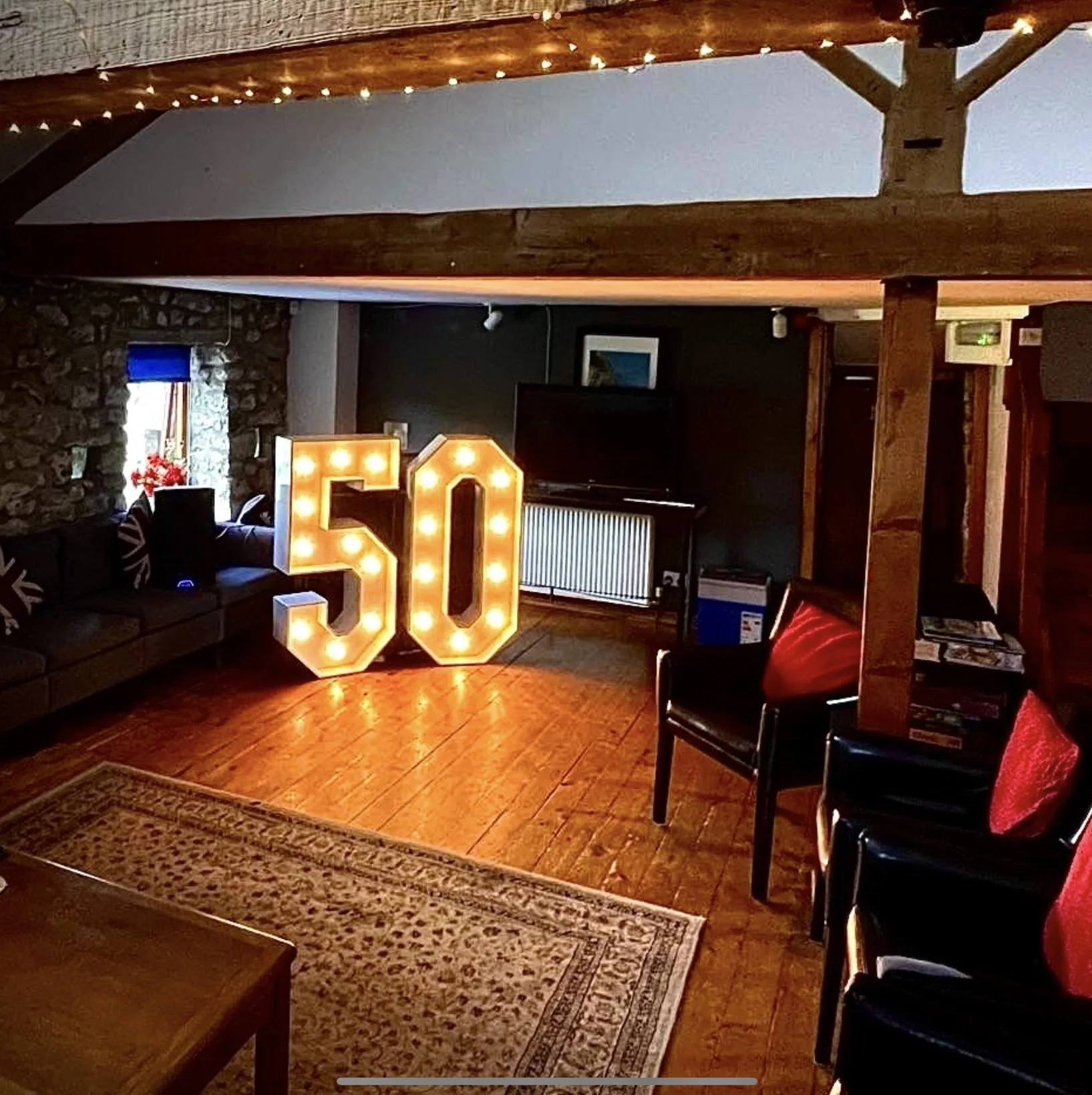Living room decorated for a 50th celebration with illuminated number '50' and red pillows on black chairs.