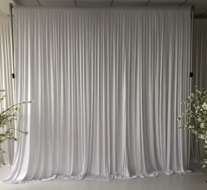 White fabric backdrop with floral arrangements on each side, likely set up for a wedding or special event.