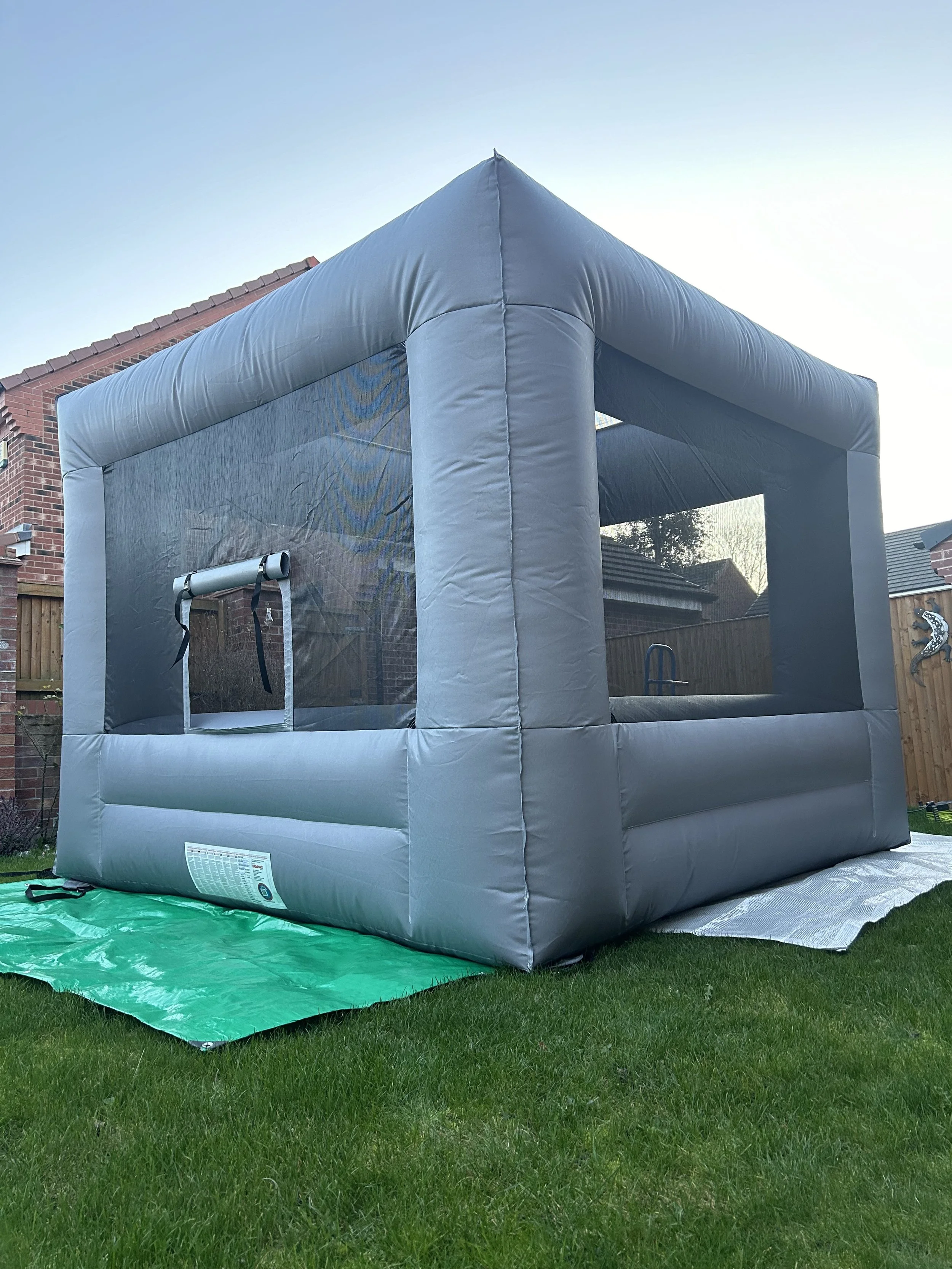 Inflatable bounce house set up in a backyard on a grassy lawn, with a blue sky overhead and houses in the background.