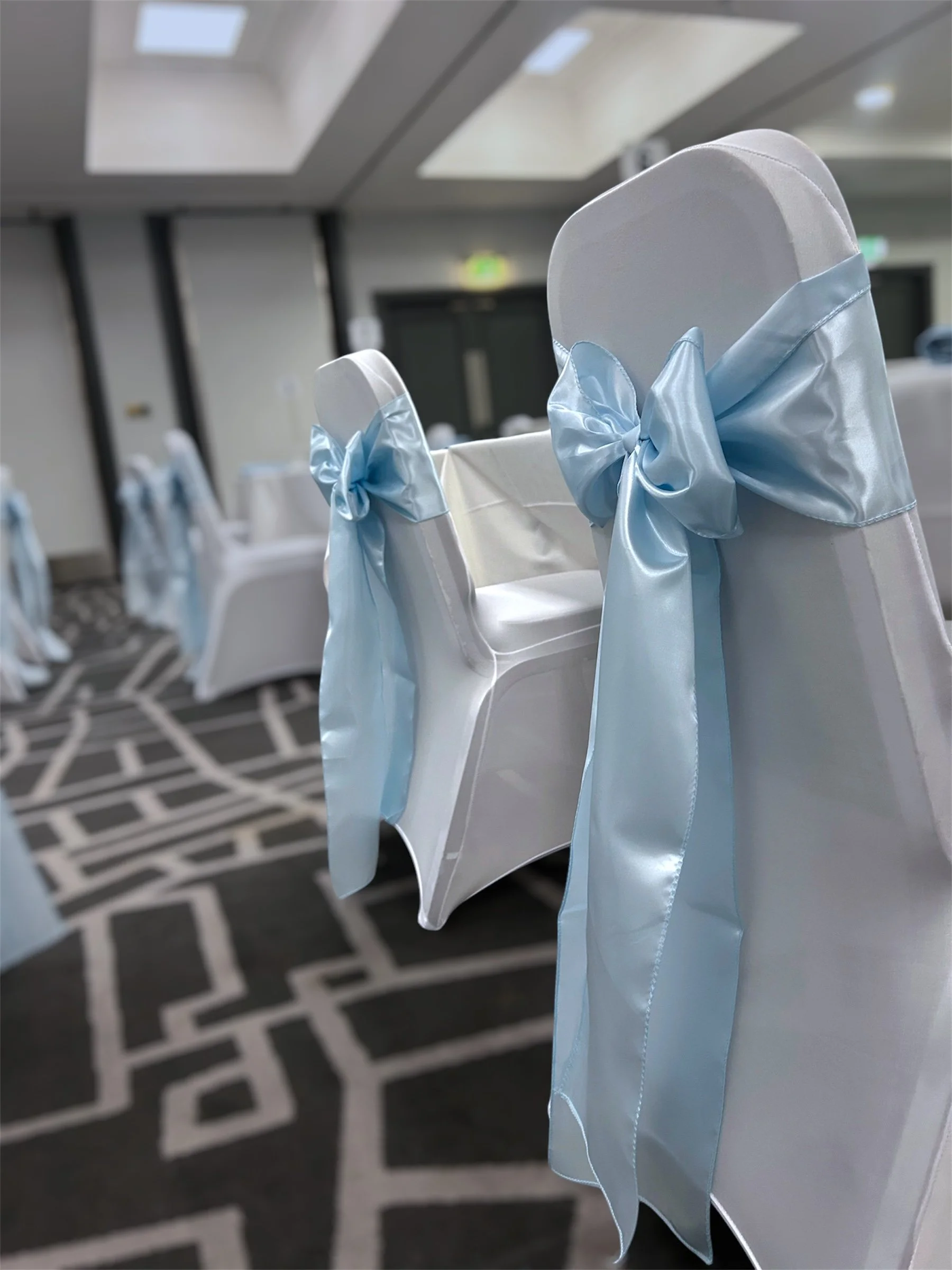 Chairs decorated with white covers and light blue satin ribbons in a banquet hall.