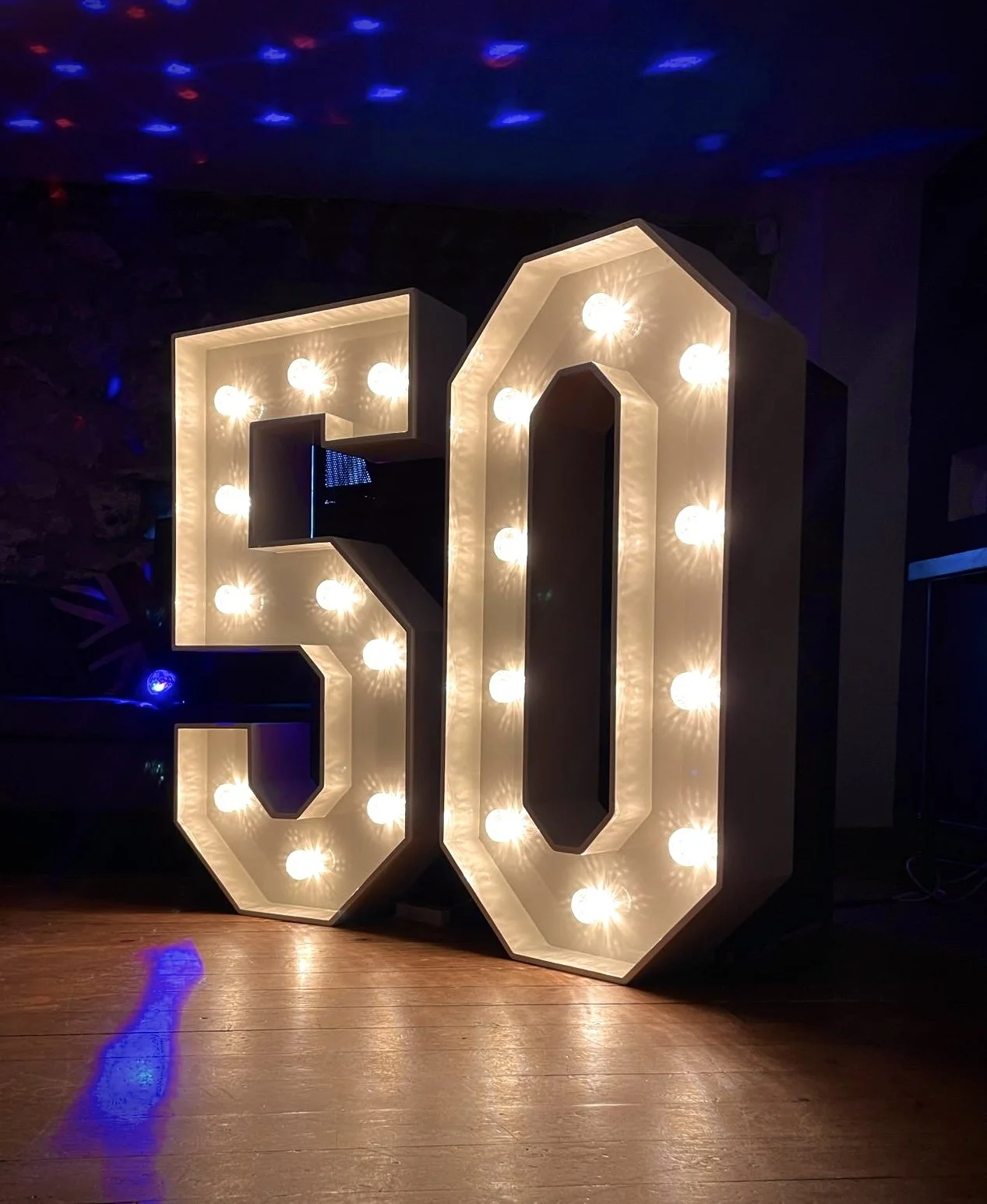 Large illuminated marquee sign with the number 30 in white lightbulbs, placed on a wooden floor in a dark room.