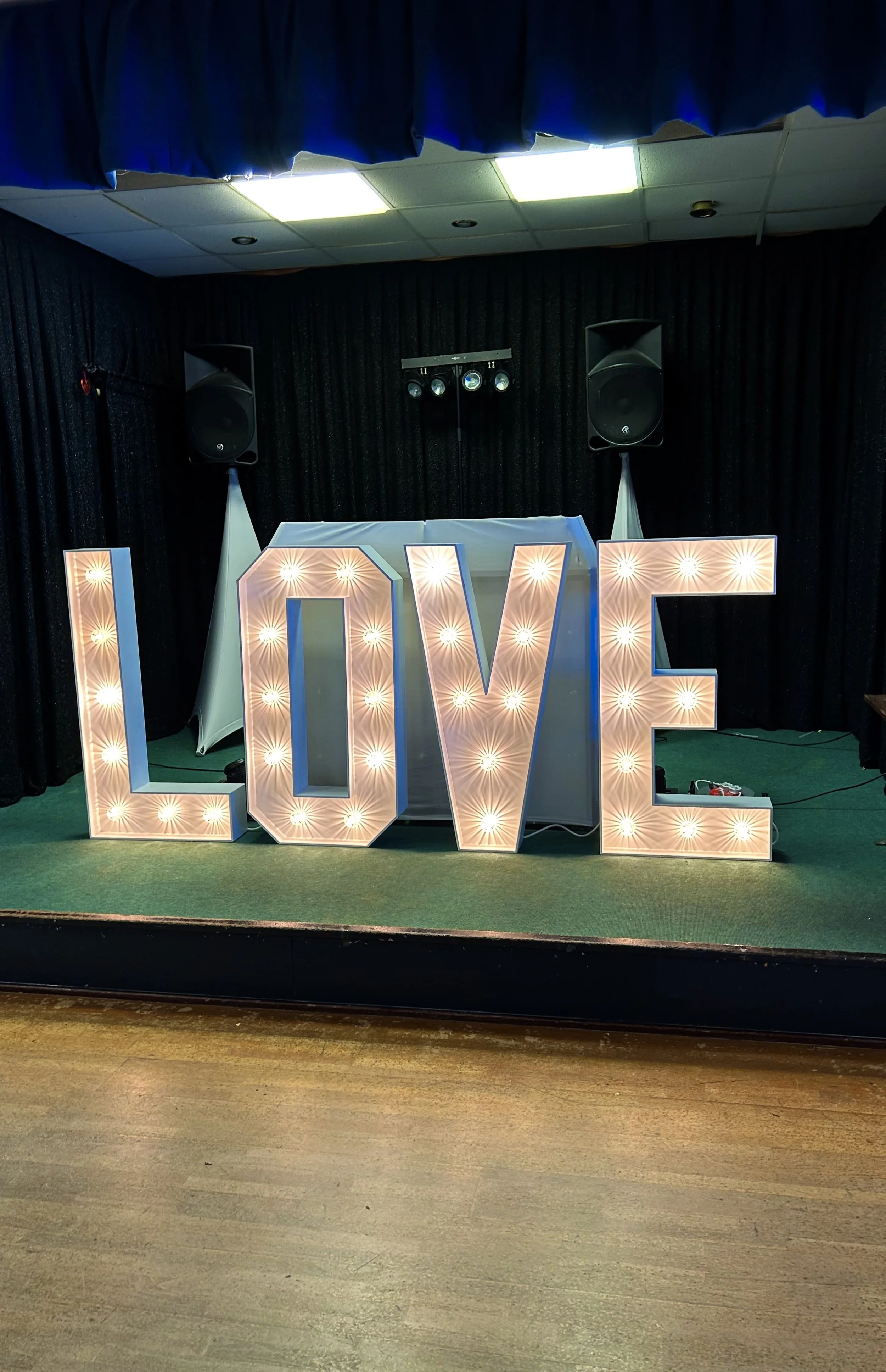 Decorative illuminated letters spelling "LOVE" on a stage with a DJ setup and black curtains.