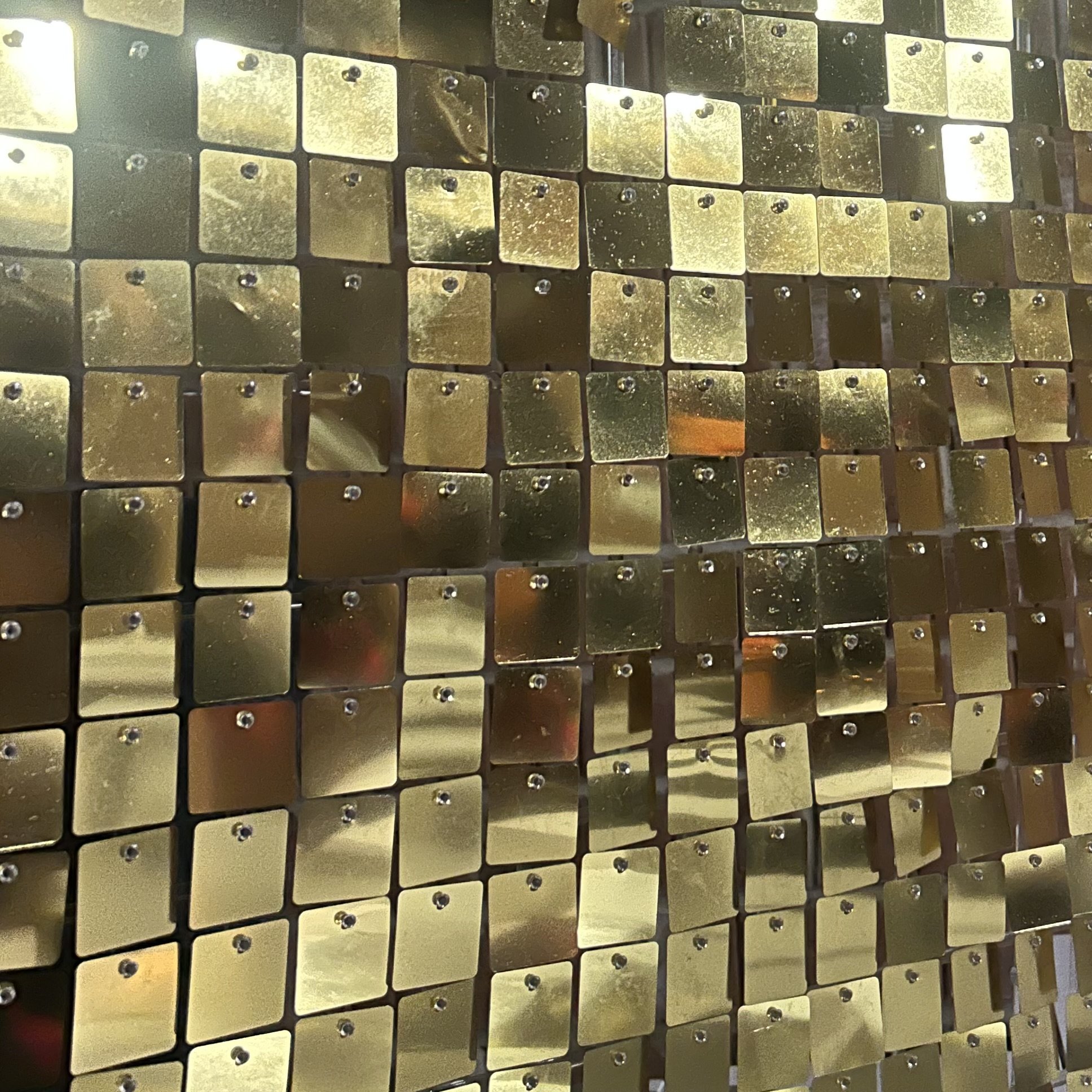 Close-up of a decorative wall composed of small, reflective, gold-colored square tiles arranged in a grid pattern.