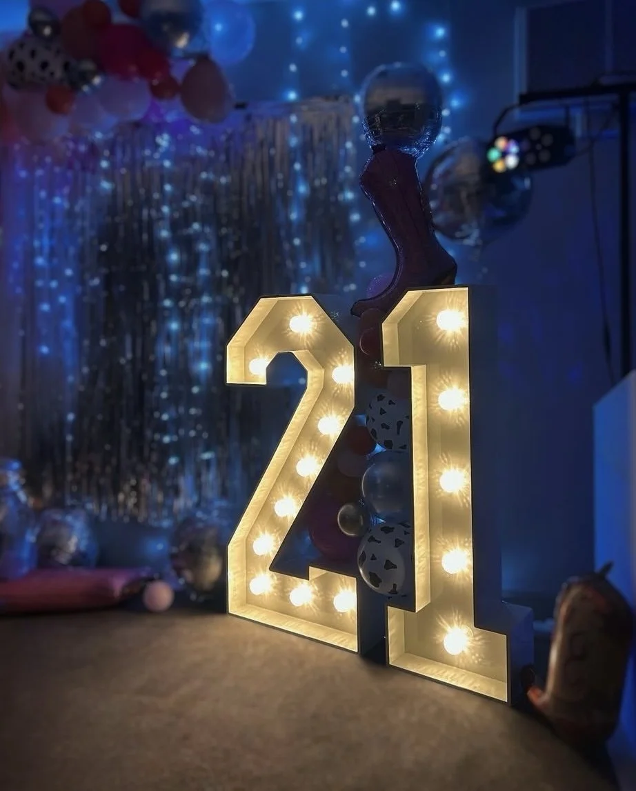 Decorative illuminated '2021' sign with balloons and balloons backdrop, blue lighting, and festive decorations.