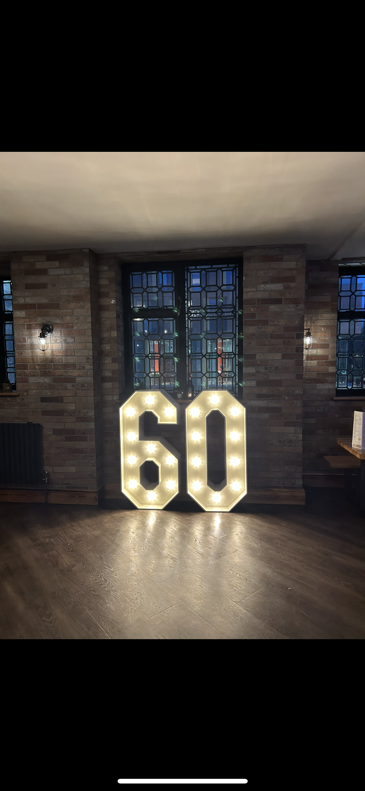 Large illuminated number '60' sign against brick wall with stained glass windows in the background.