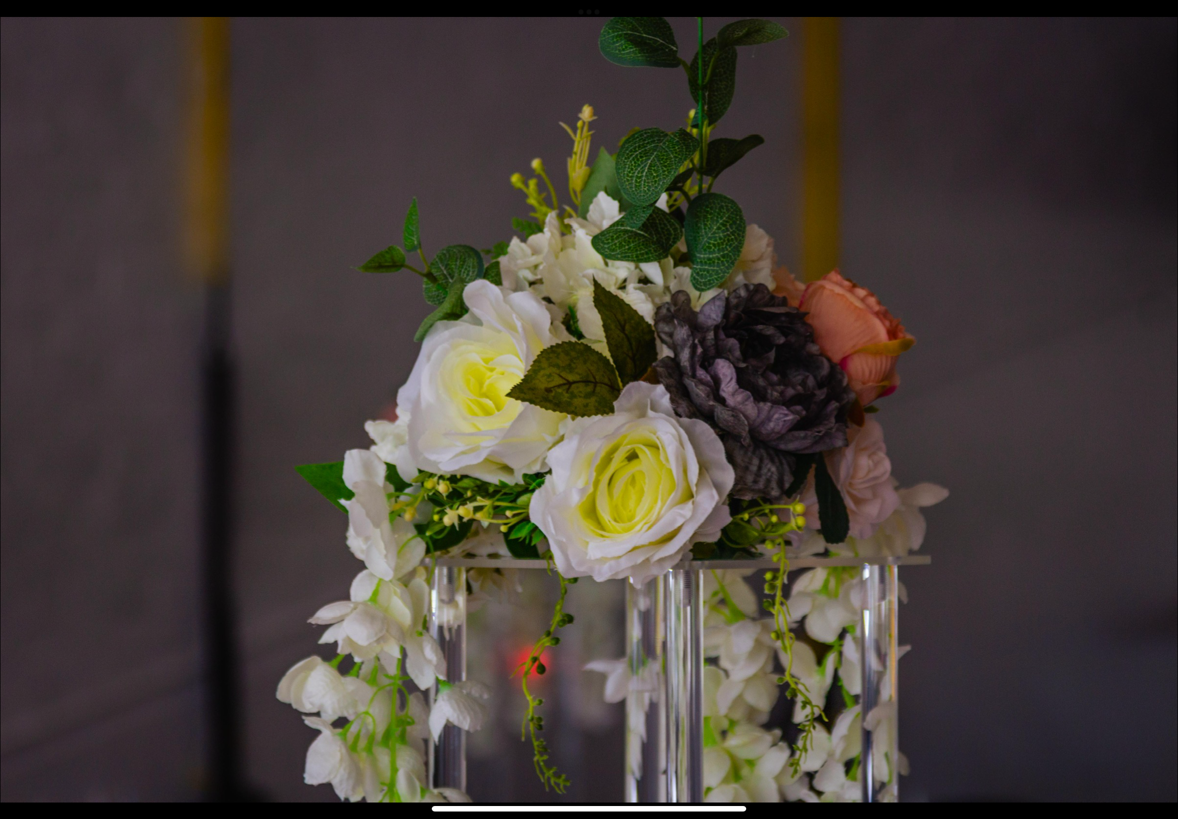 Elegant flower arrangement with white roses, purple flowers, pink roses, and green foliage in a glass stand.