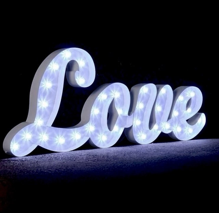 Lit decorative sign spelling 'Love' in cursive with small lights, on a dark background.
