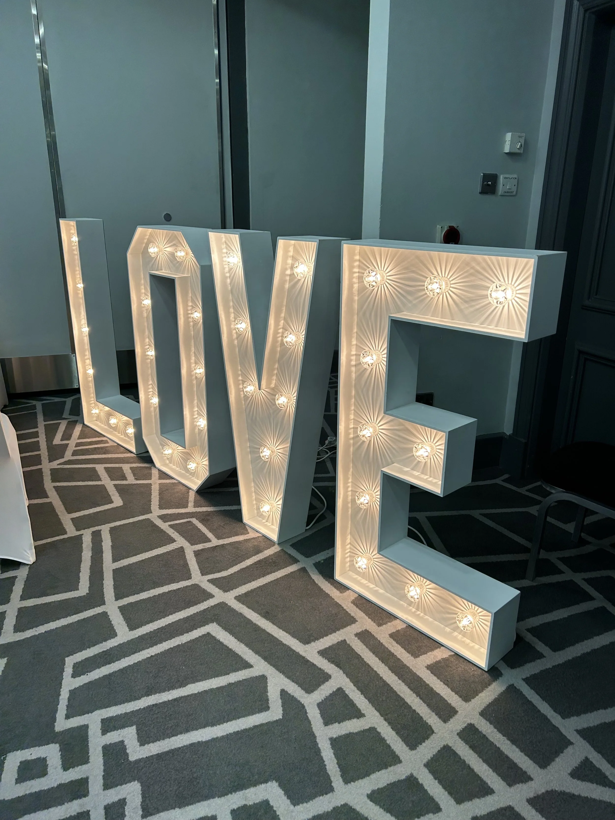 Decorative white letter sign spelling 'LOVE' with illuminated bulbs inside a modern room.