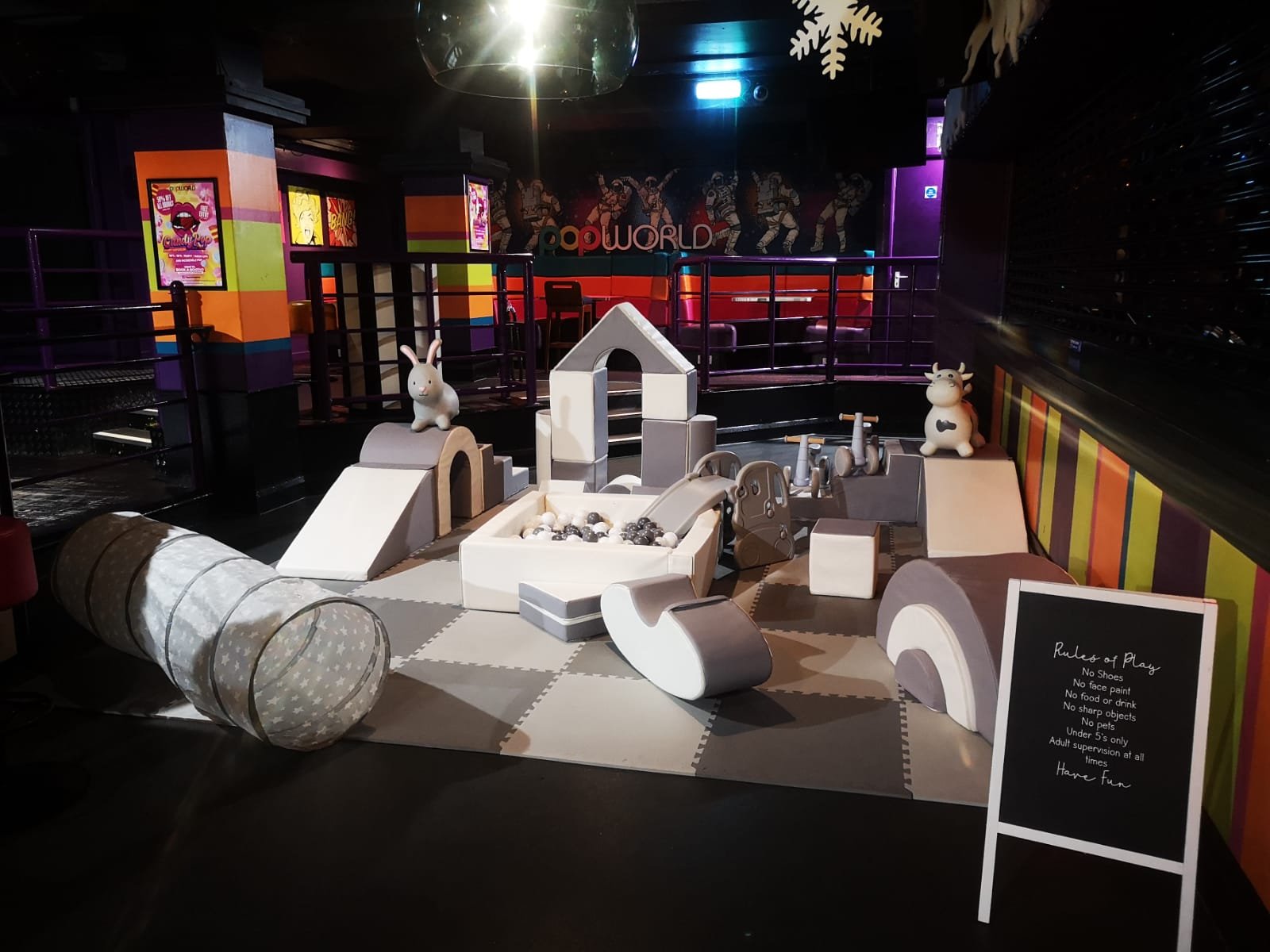 Indoor play area with various soft play structures including a tunnel, slide, and animal figures, in a colorful entertainment venue.