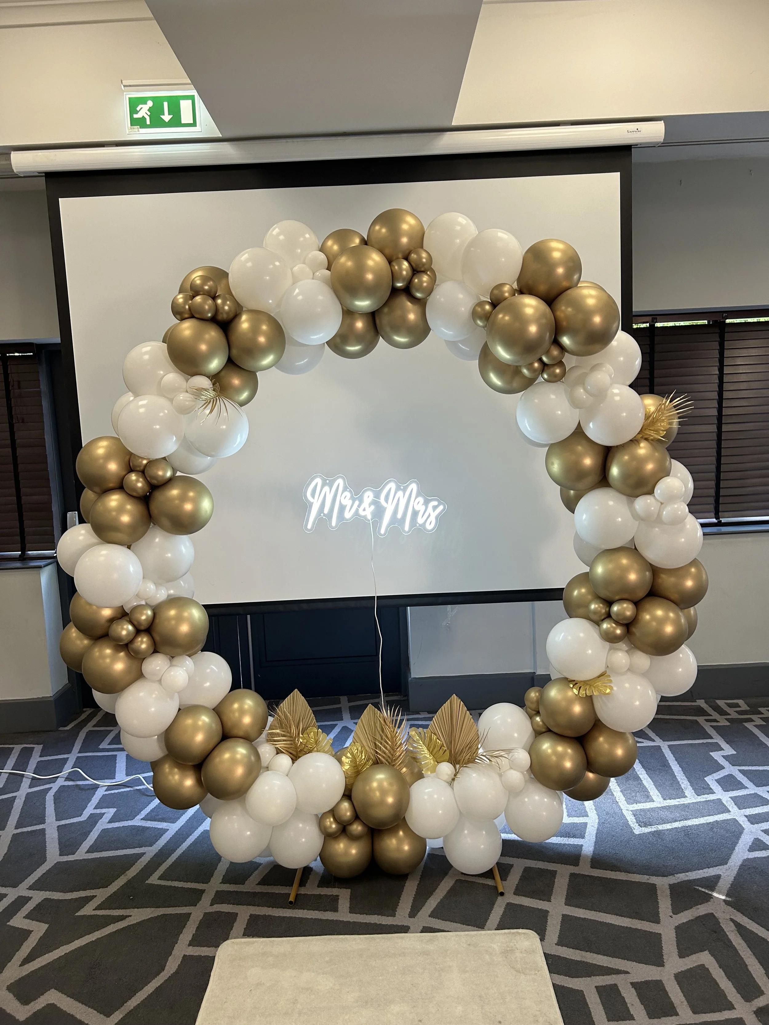 Decorative balloon arch in gold and white surrounding a sign that says "Wou & Mox" for a celebration or event.