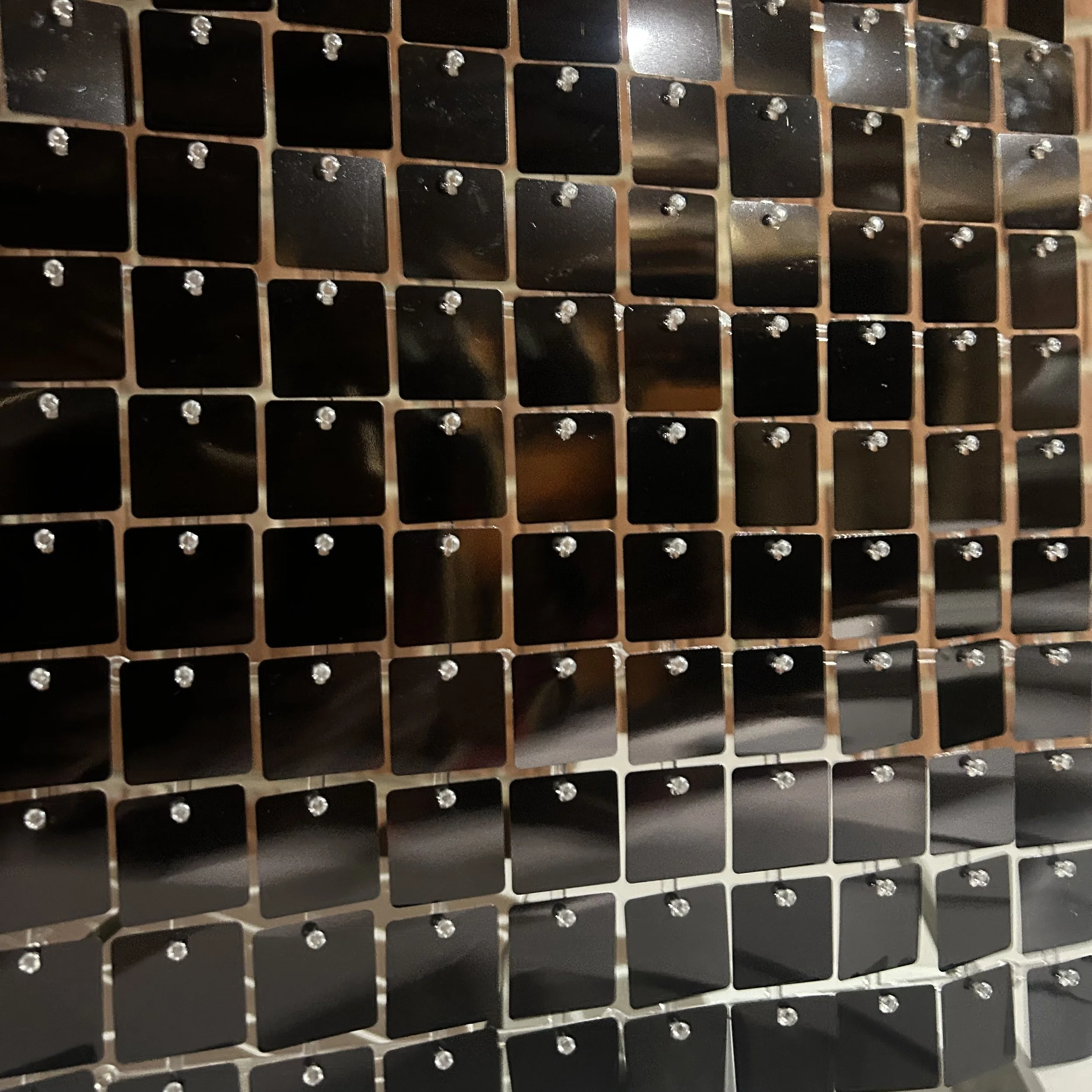 Close-up of a metallic grill with square black panels and small shiny bolts or screws at the corners of each panel.