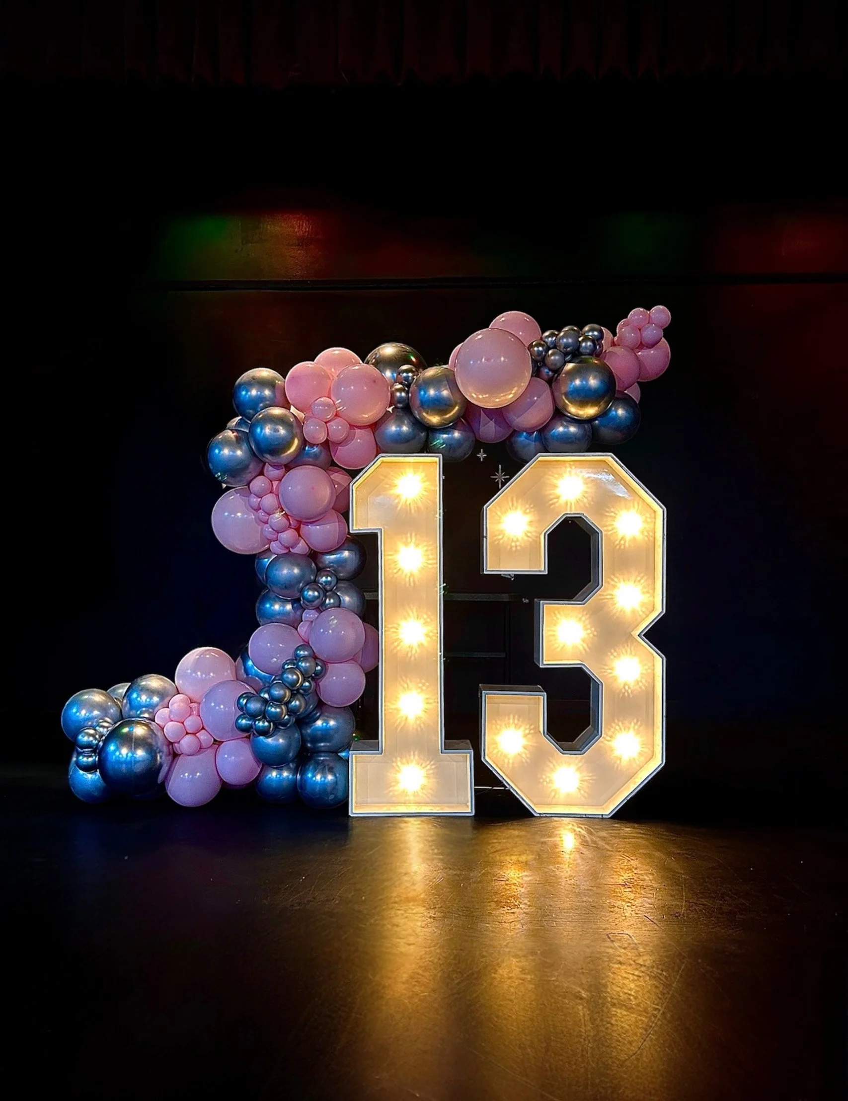 Decorative anniversary display with illuminated number 13 and pink, purple, and metallic balloons arranged around it.
