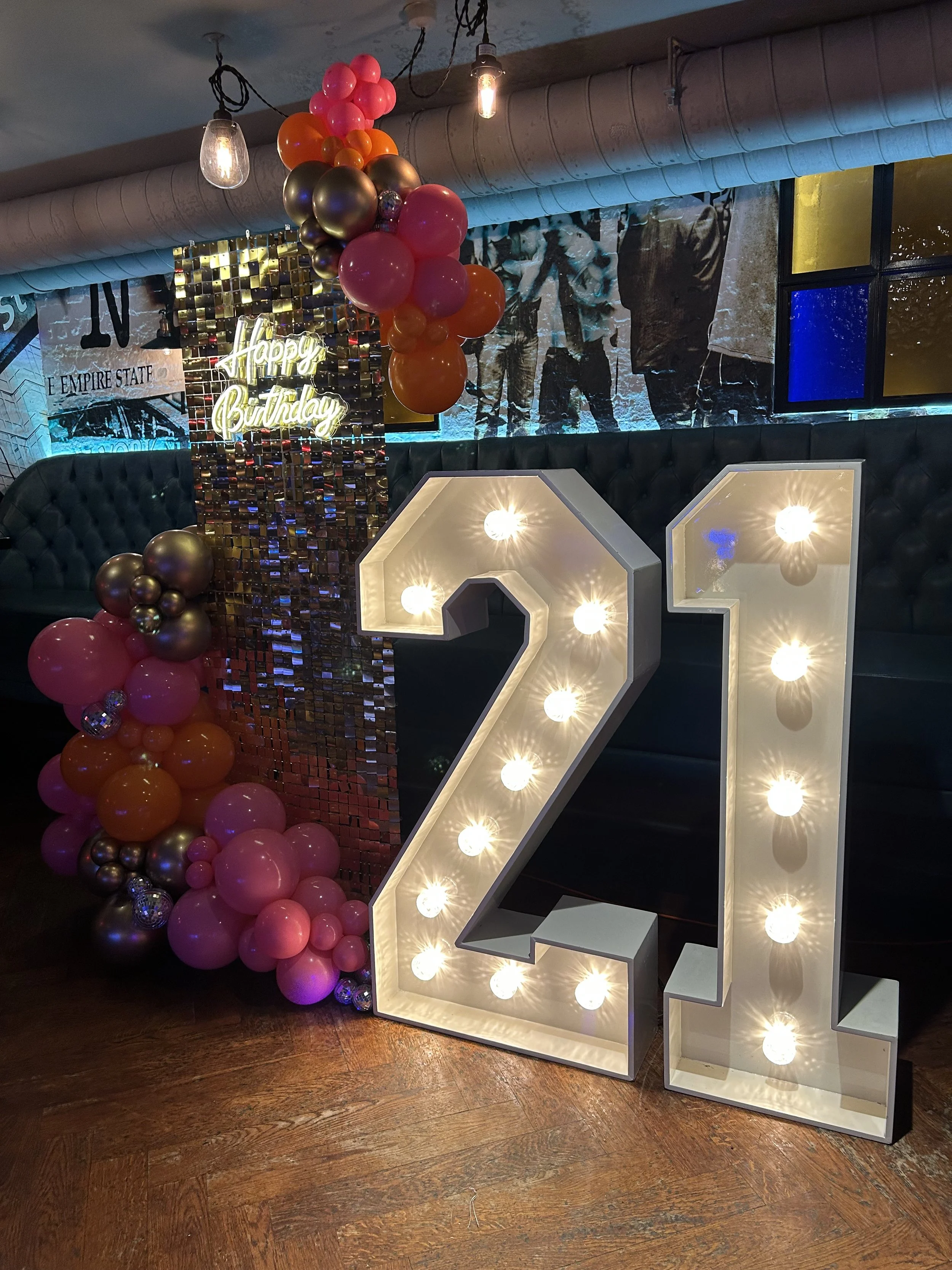 Large illuminated number 21 with balloons and a "Happy Birthday" sign in a decorated indoor venue.