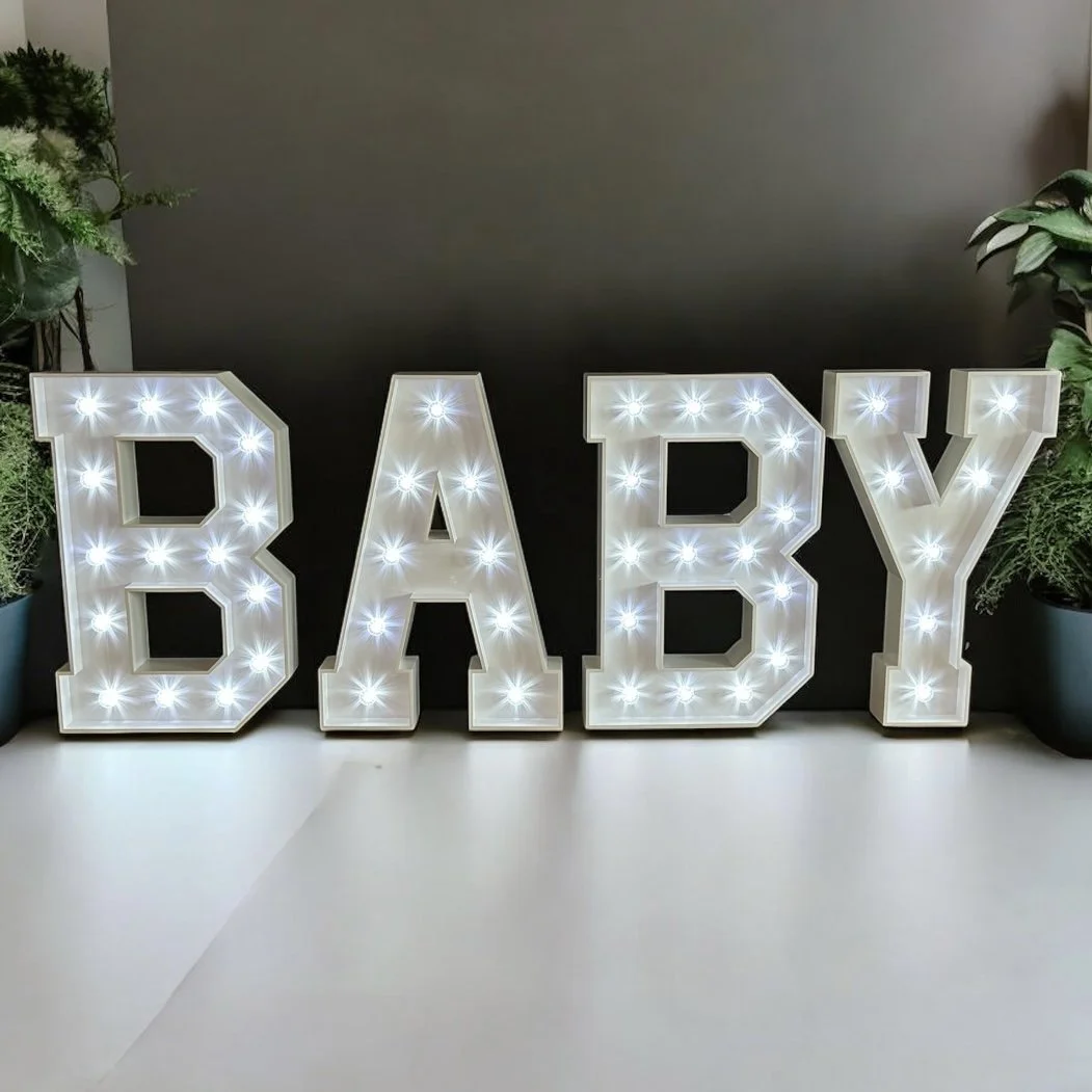Large illuminated light-up letters spelling 'BABY' on a wooden floor in front of a dark stage area.