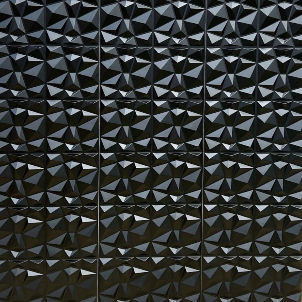 Close-up view of a black, geometric, textured wall composed of triangular facets arranged in a repeating pattern.