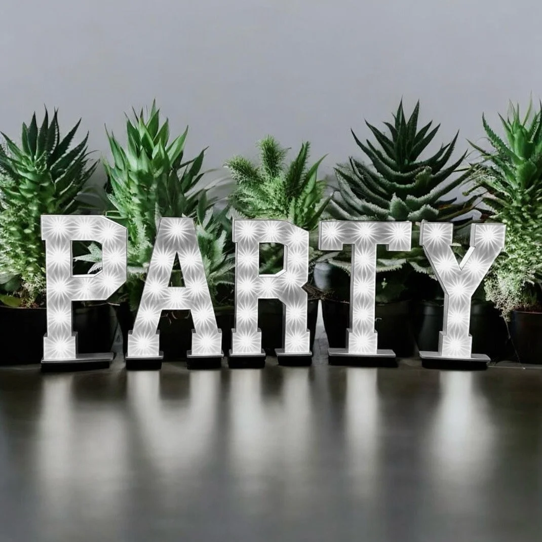 Decorative illuminated sign spelling 'PARTY' with potted green plants in the background.