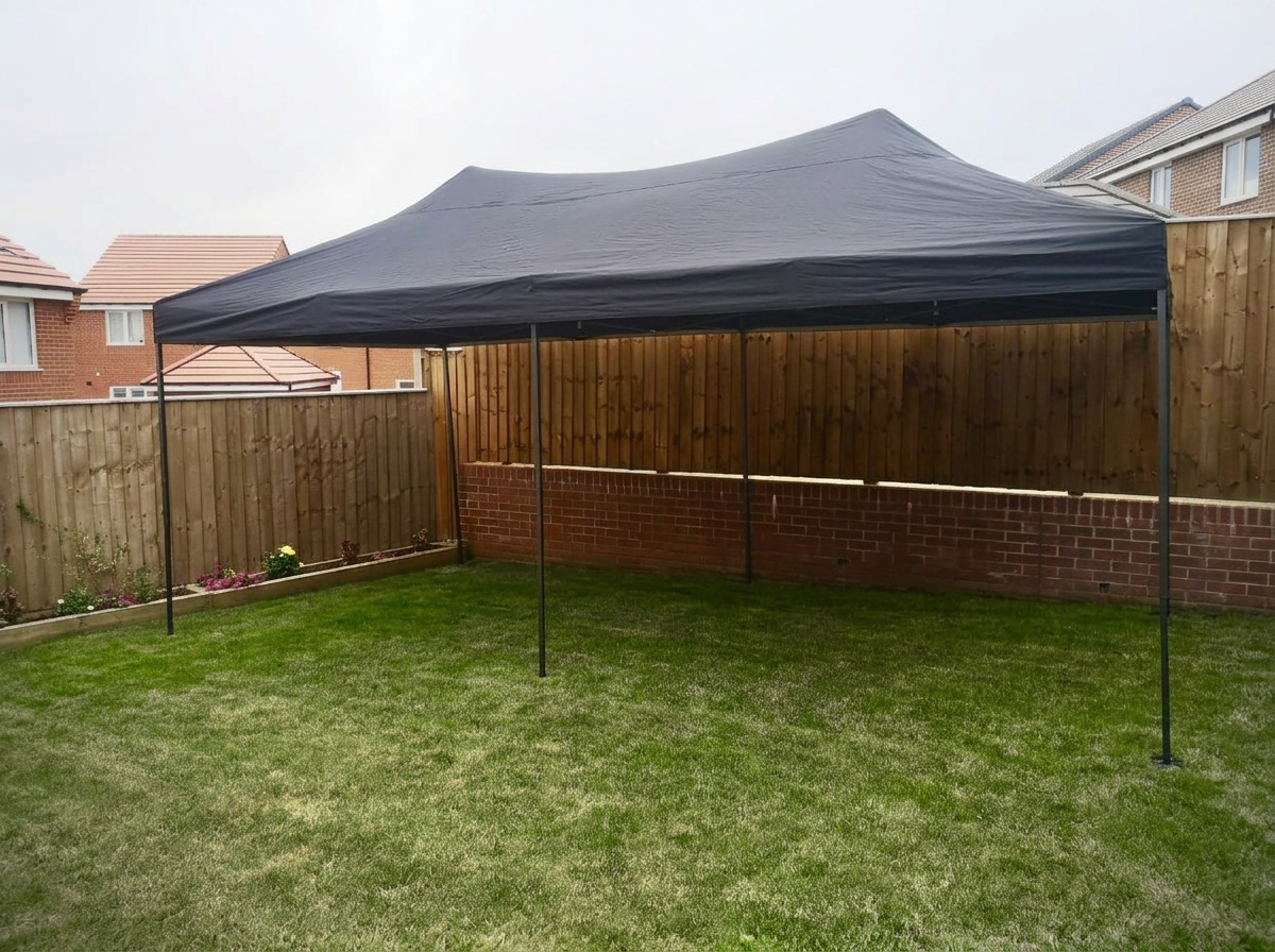 Black outdoor canopy tent set up on a grassy backyard with a wooden fence and brick wall support.