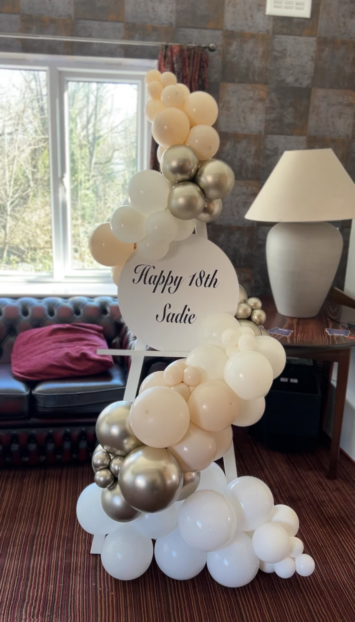 Balloon arrangement with white, silver, and blush-colored balloons and a sign reading "Happy 18th Sadie" for an birthday celebration.
