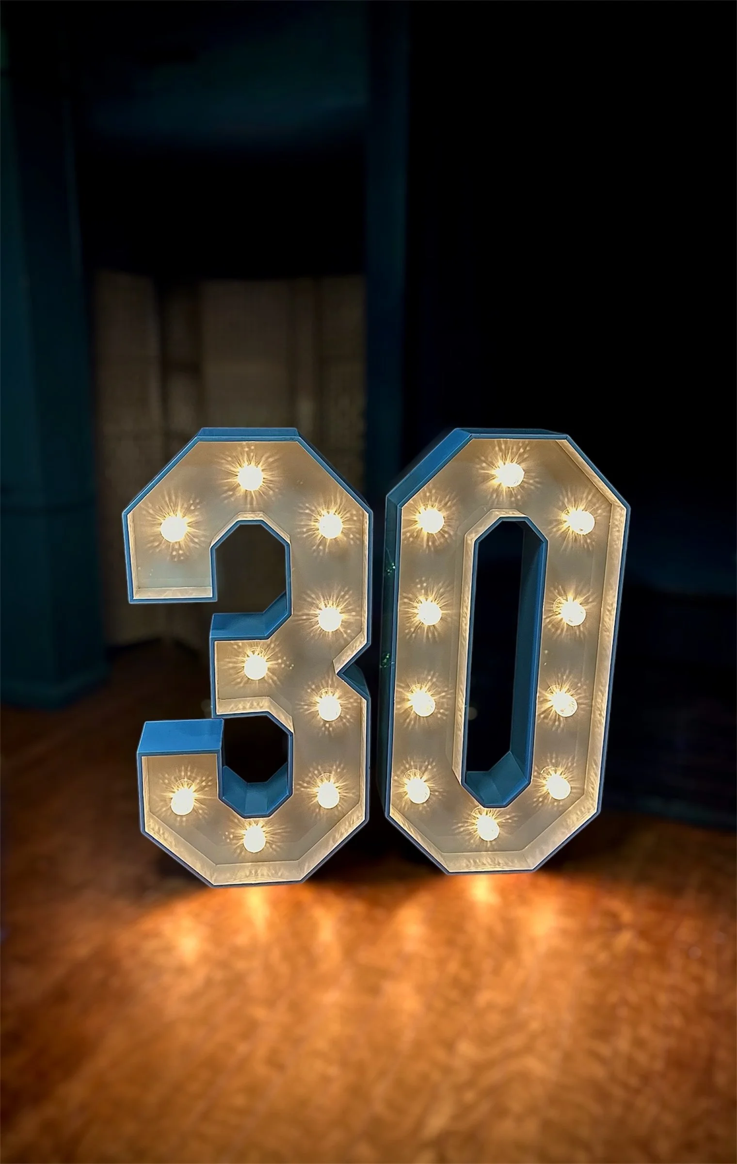 Illuminated decorative LED numbers displaying '30' on a wooden surface in a dark room.