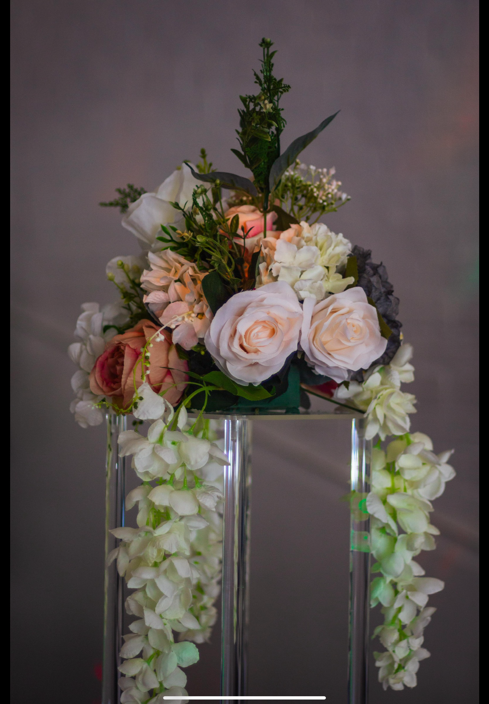 A floral arrangement with white and blush pink roses, white hydrangeas, and greenery on a metal stand with hanging white flowers.