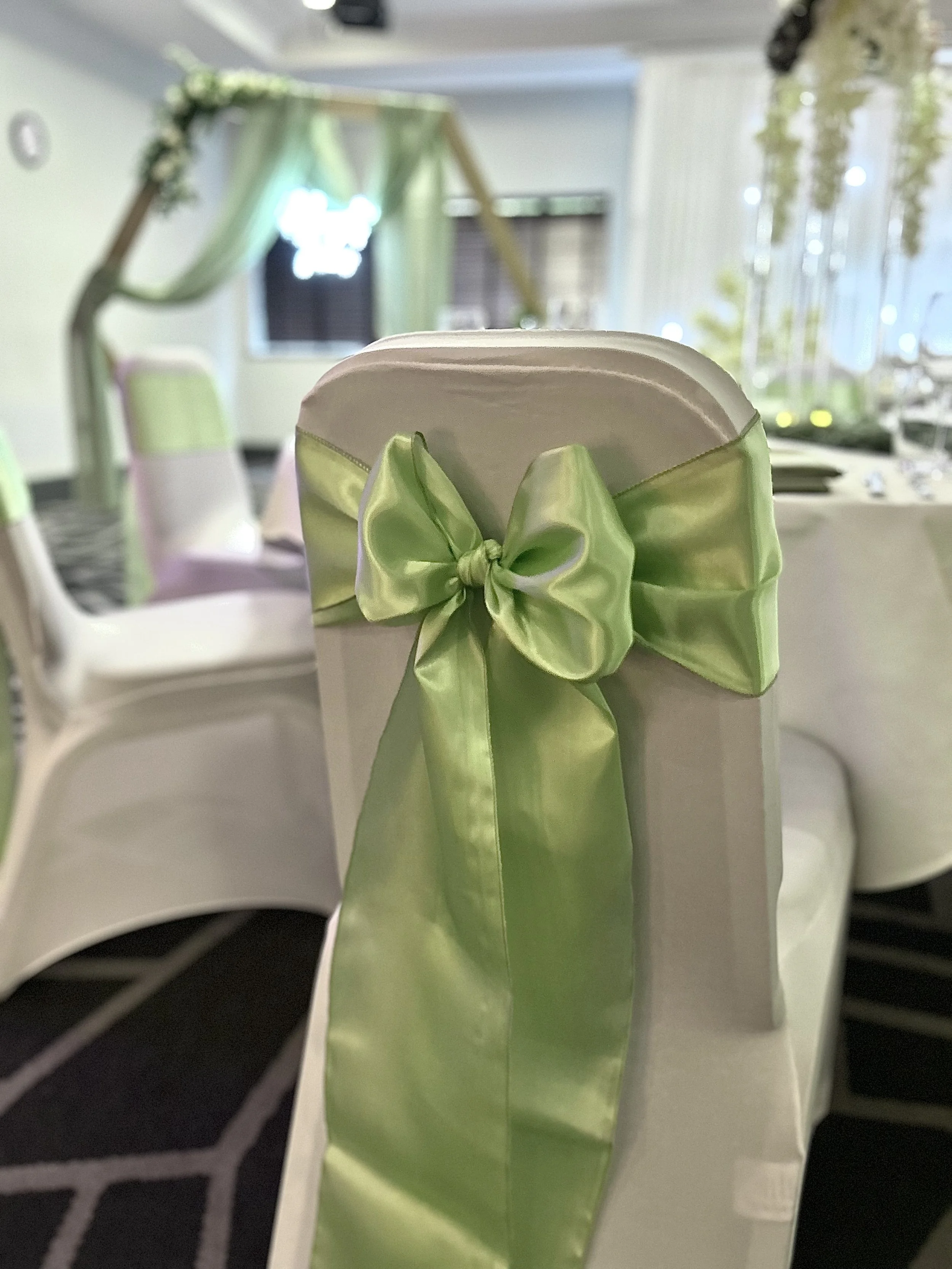 White banquet chairs decorated with light blue satin sashes tied into bows, set up for a formal event in a banquet hall.