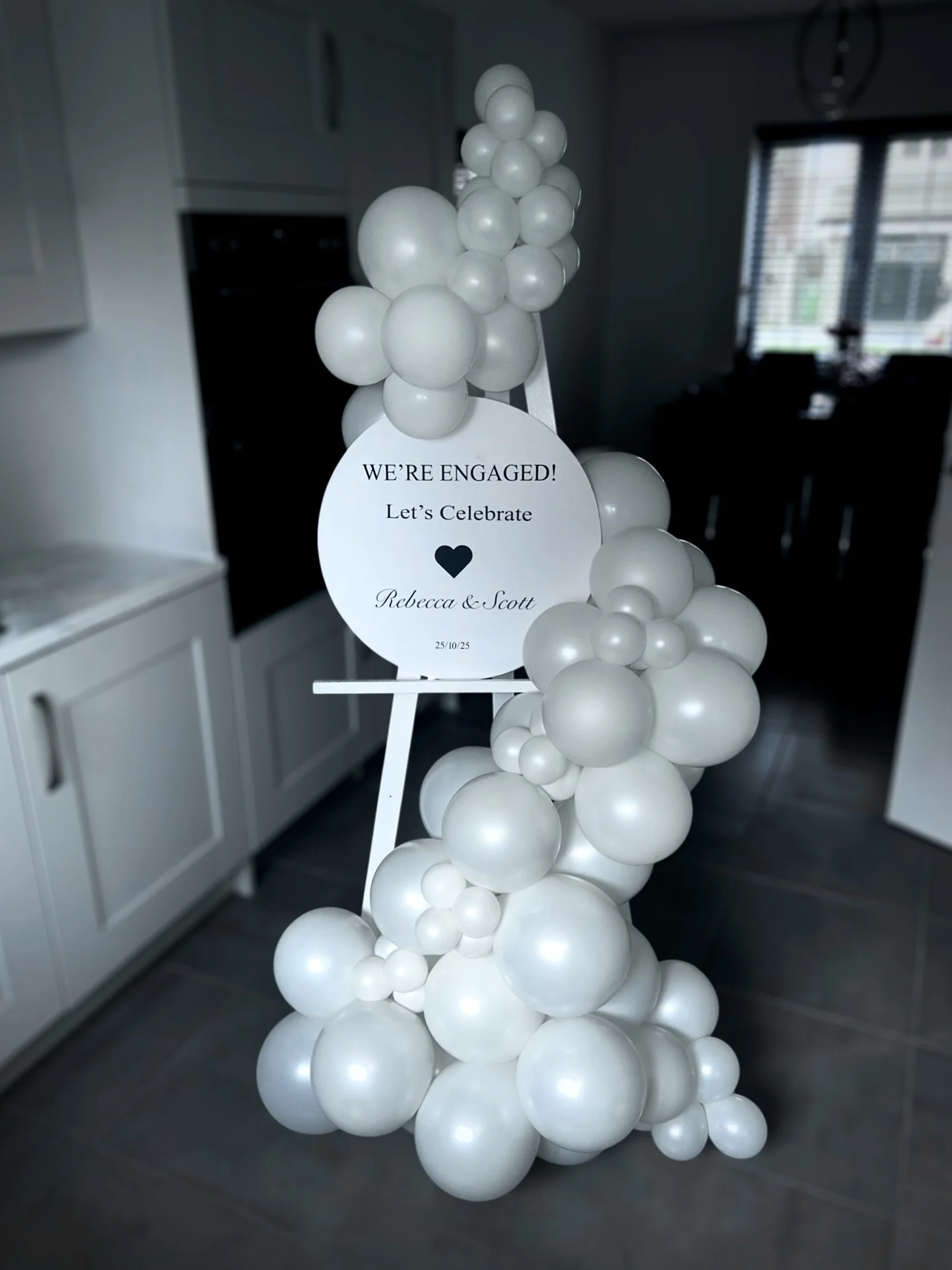 Black and white balloon display with a circular sign announcing engagement celebration for Rebecca and Scott, dated 25/10/25.