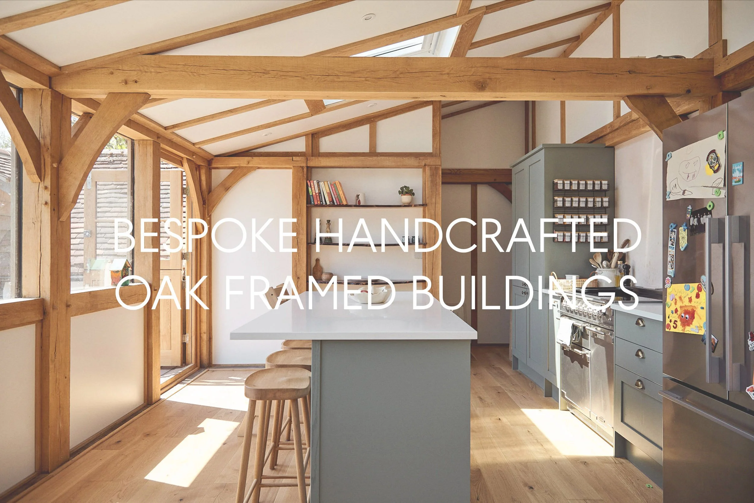 Modern kitchen in an oak framed extension with wooden beams, white countertop island with stools, light blue cabinets, stainless steel appliances, and shelves with books and decor, illuminated by natural light from large windows.