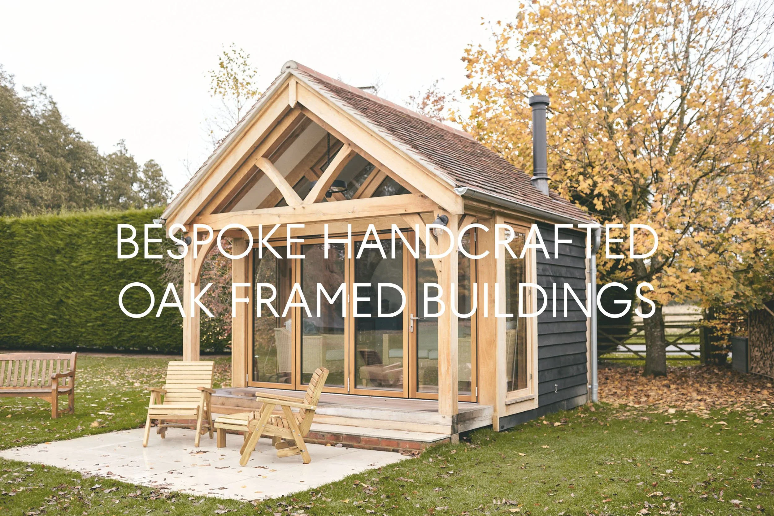 A small, oak-framed building with large glass sliding doors and a pitched roof, situated outdoors on a grassy area with autumn trees in the background.