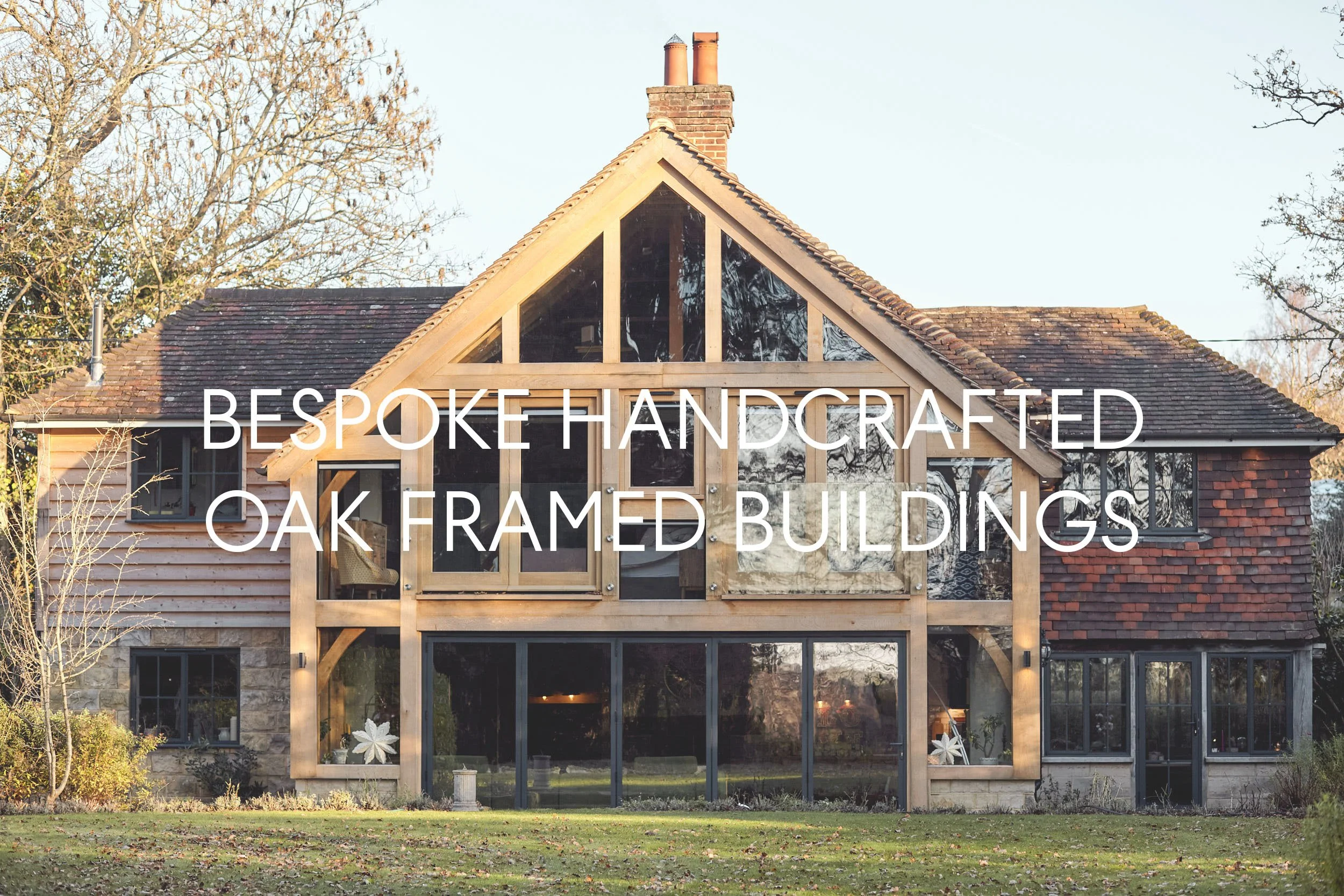 A house with a combination of old brick and new contemporary two storey oak framed extension, featuring large windows and a steeply sloped roof, set against a background of trees.