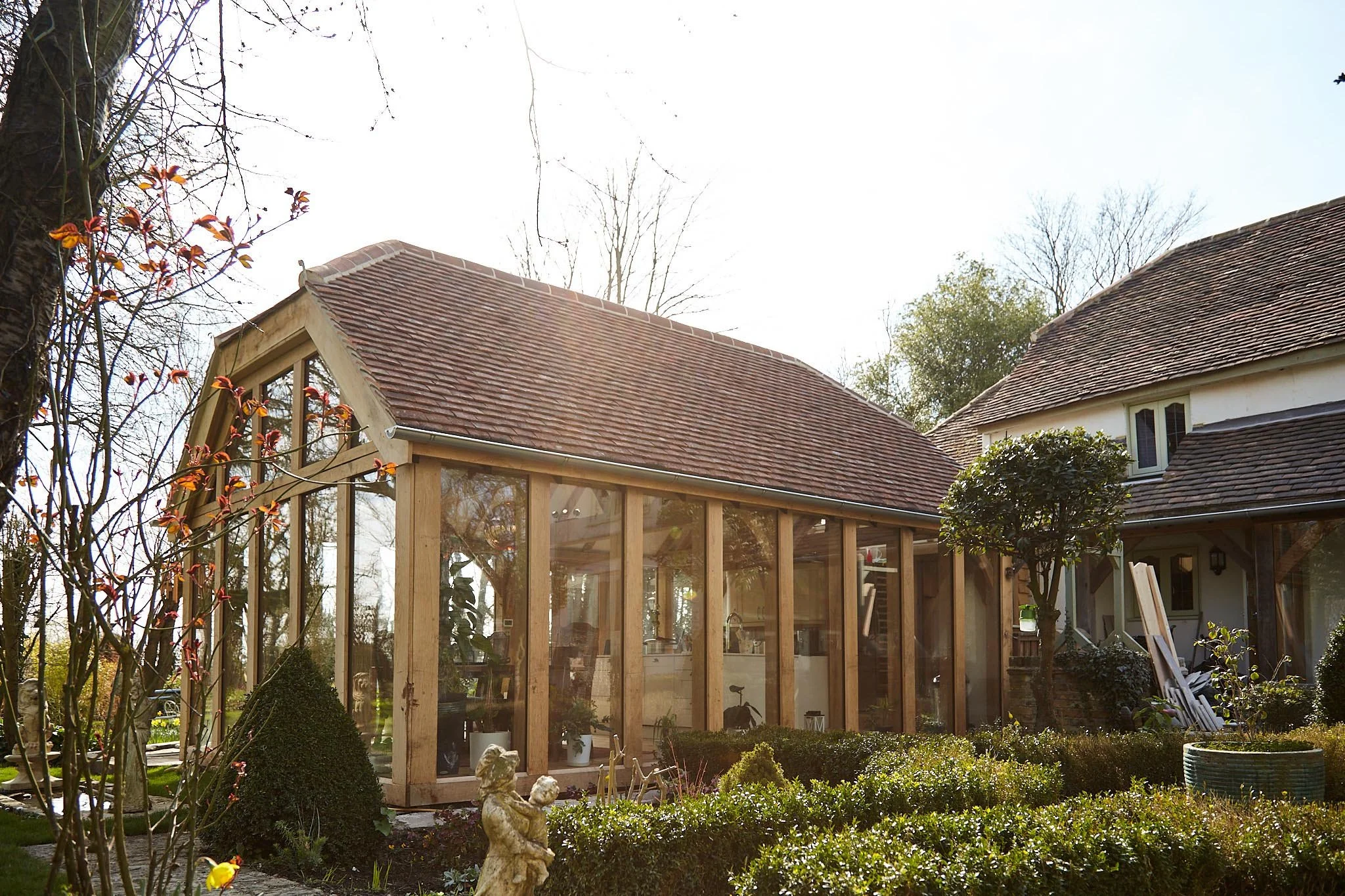 A house with a glazed oak framed sunroom extension and a garden with bushes and small trees.