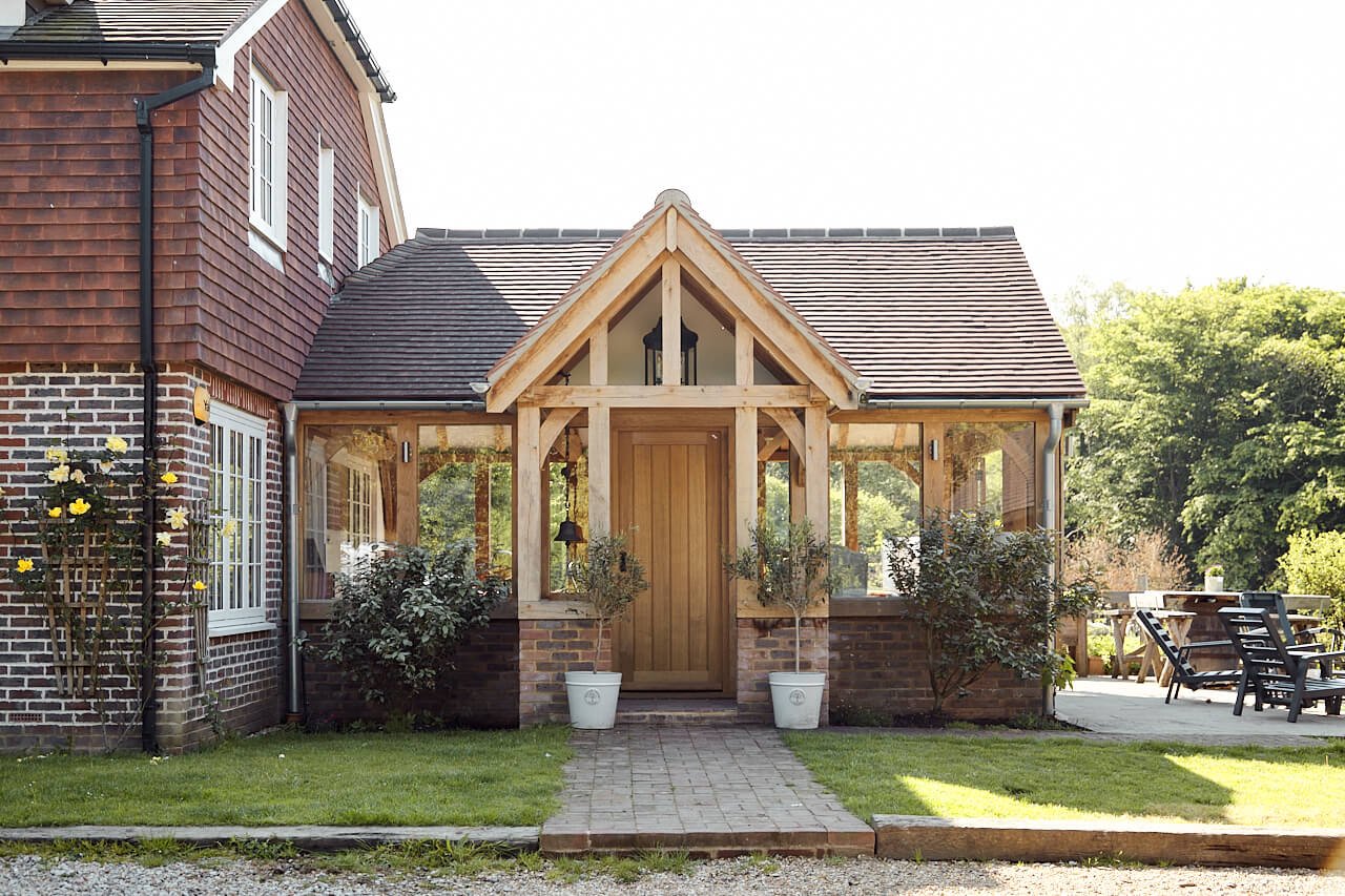 A house with a brick exterior and an oak framed porch and extension, with a gabled roof, and an outdoor seating area to the right.