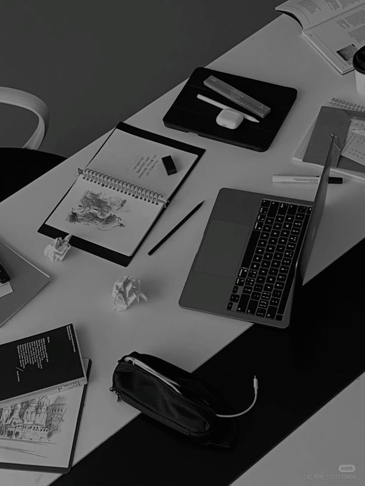 A cluttered desk with a laptop, notebooks, crumpled paper, a pencil, a pen, a box of markers, an eraser, and various papers.