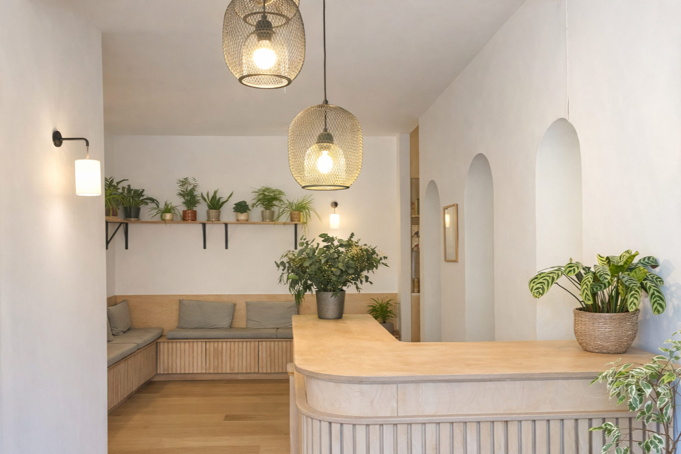 Interior of a cosy room with white walls, wooden furniture and multiple potted plants on the shelves and countertops. There are hanging pendant and wall lights, creating a warm ambiance.