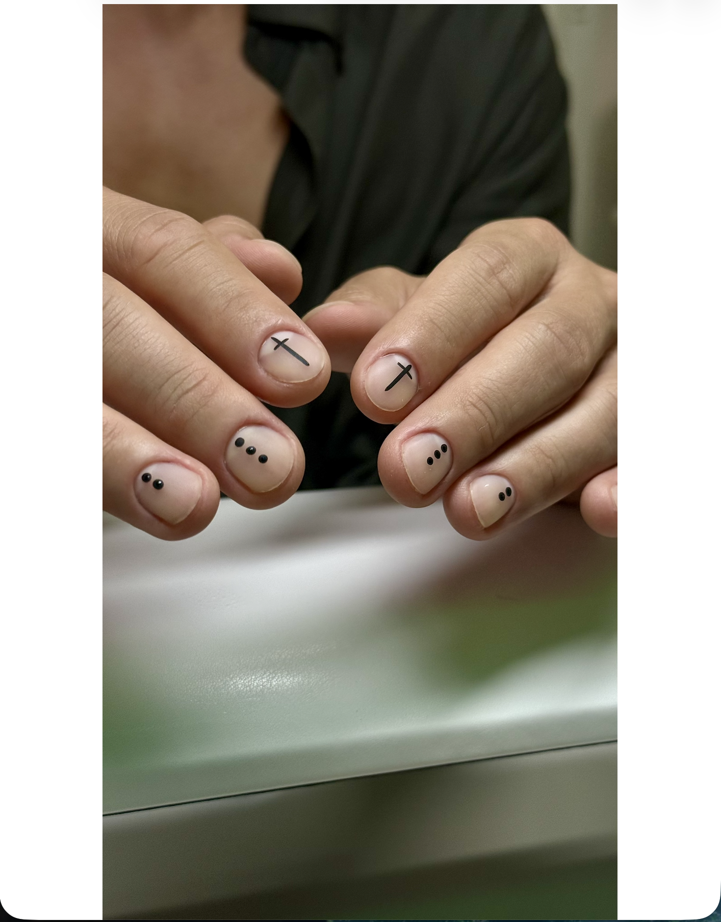 Close-up of hands with minimalistic nail art, featuring small black crosses and dots on natural nails.
