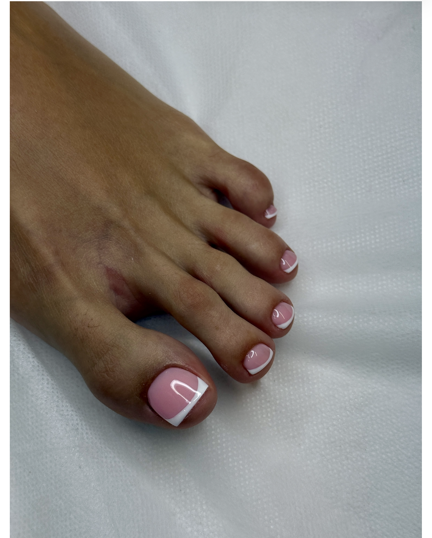 A hand with pink nails featuring white tips and a curved white line detail on each fingernail, resting on a white textured surface.
