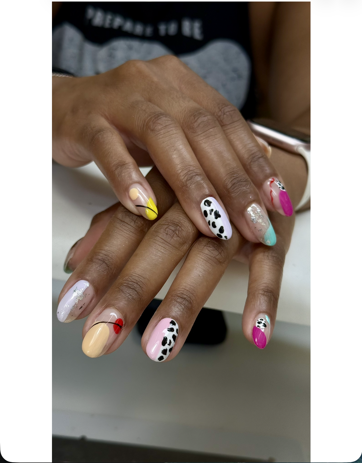 Close-up of hands with colorful, decorated nails featuring various patterns including leopard print, solid colors, and abstract designs.