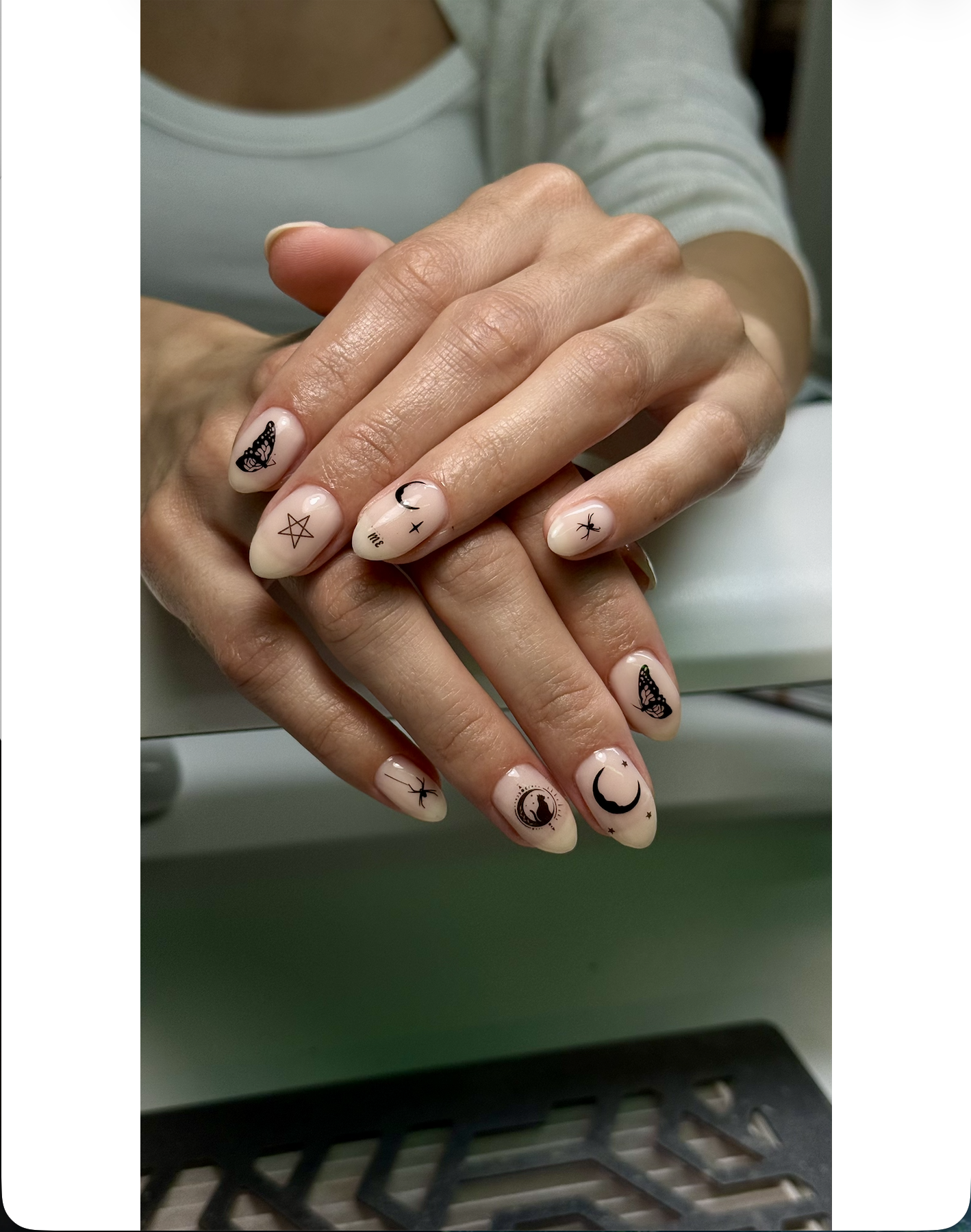 Close-up of hands with moon, star, butterfly, and other celestial-themed nail art designs.