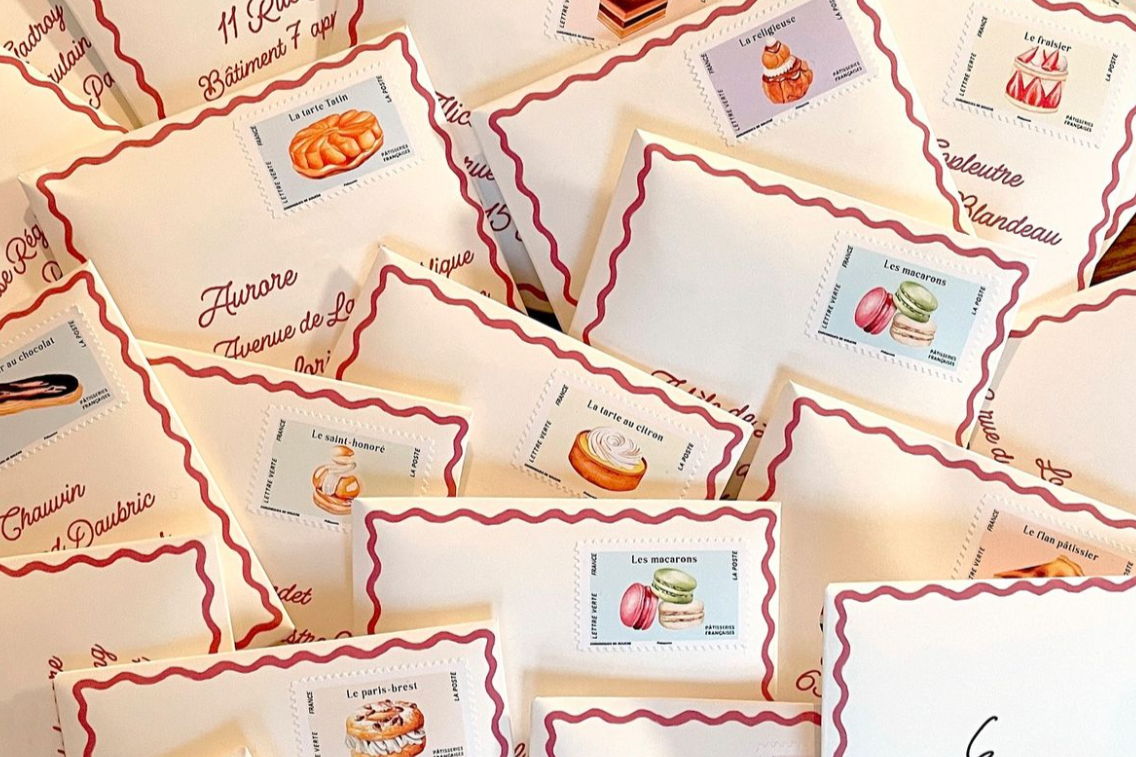 Several small cream-colored envelopes decorated with red wavy borders, each featuring a French pastry or macaron illustration and French text labels.