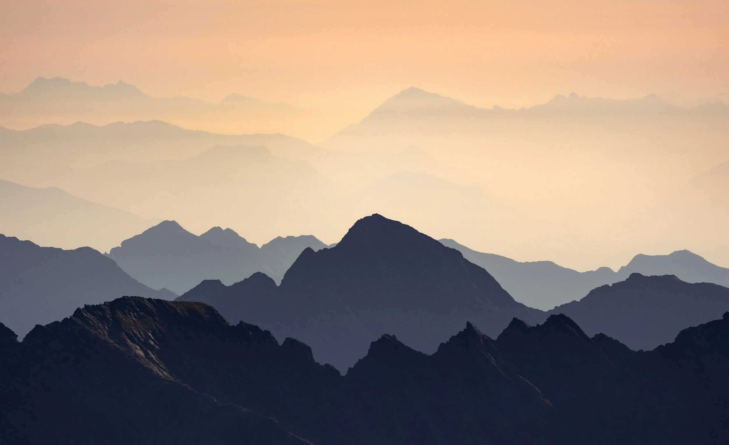 Layers of mountain silhouettes at sunset with soft pastel sky.